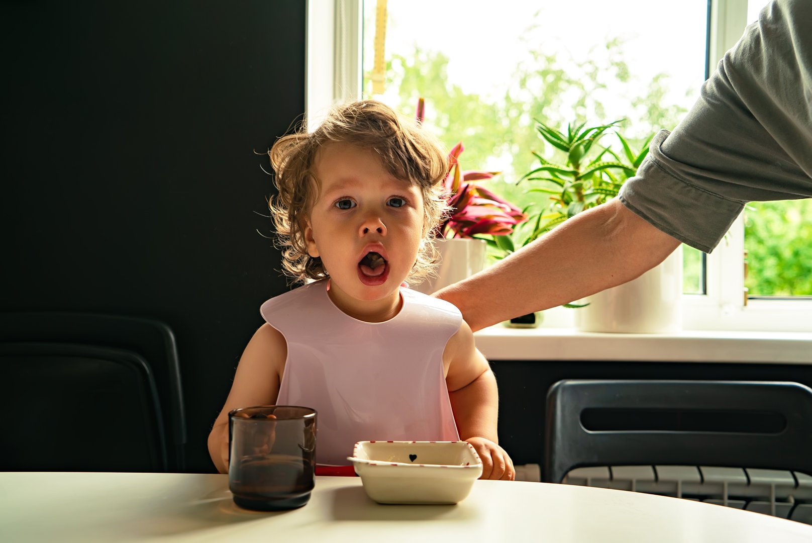 Portrait of a small child choked on food eating in the kitchen and a parent slaps his hand on the back