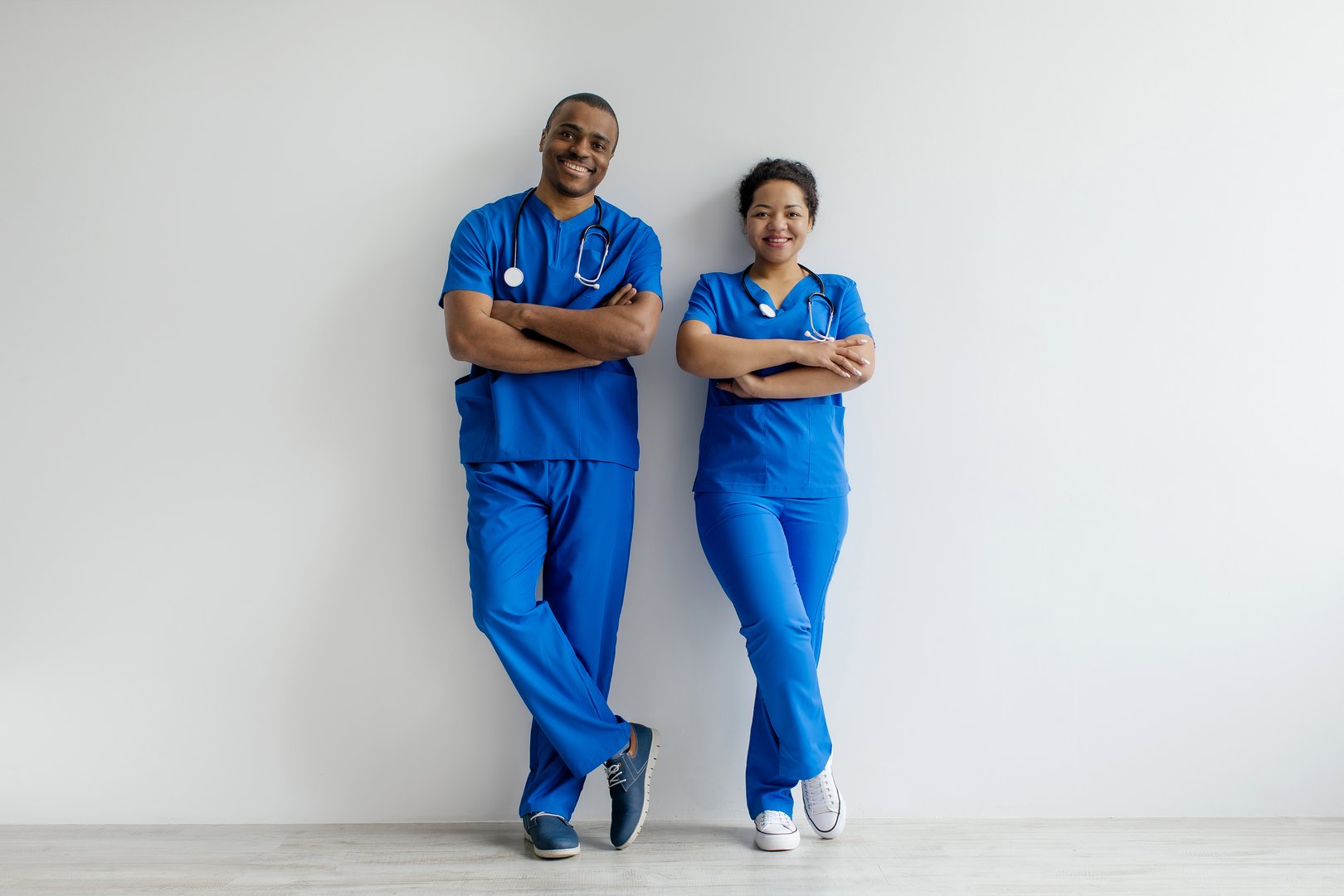 Portrait of two African American healthcare professionals in blue scrubs, confidently standing with arms crossed and smiling