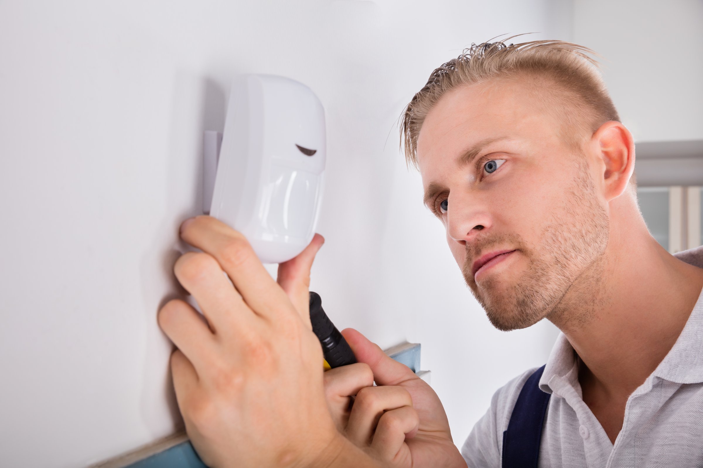 Male Electrician Installing Security System Door Sensor On Wall