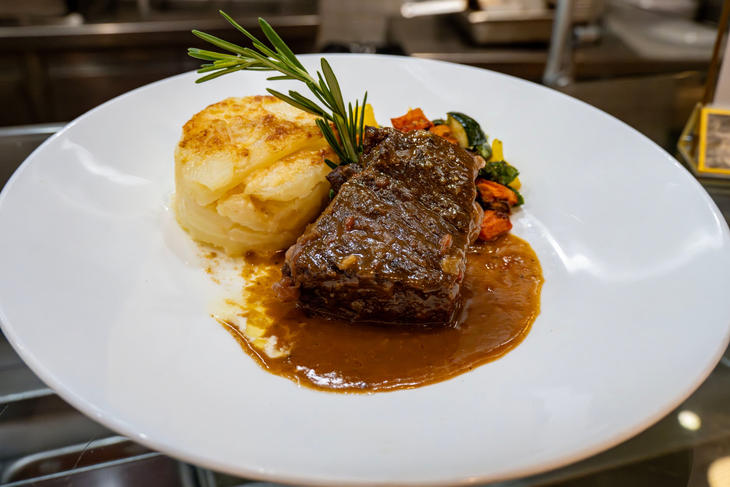 A plat of short ribs with roasted vegetables and au gratin potatoes