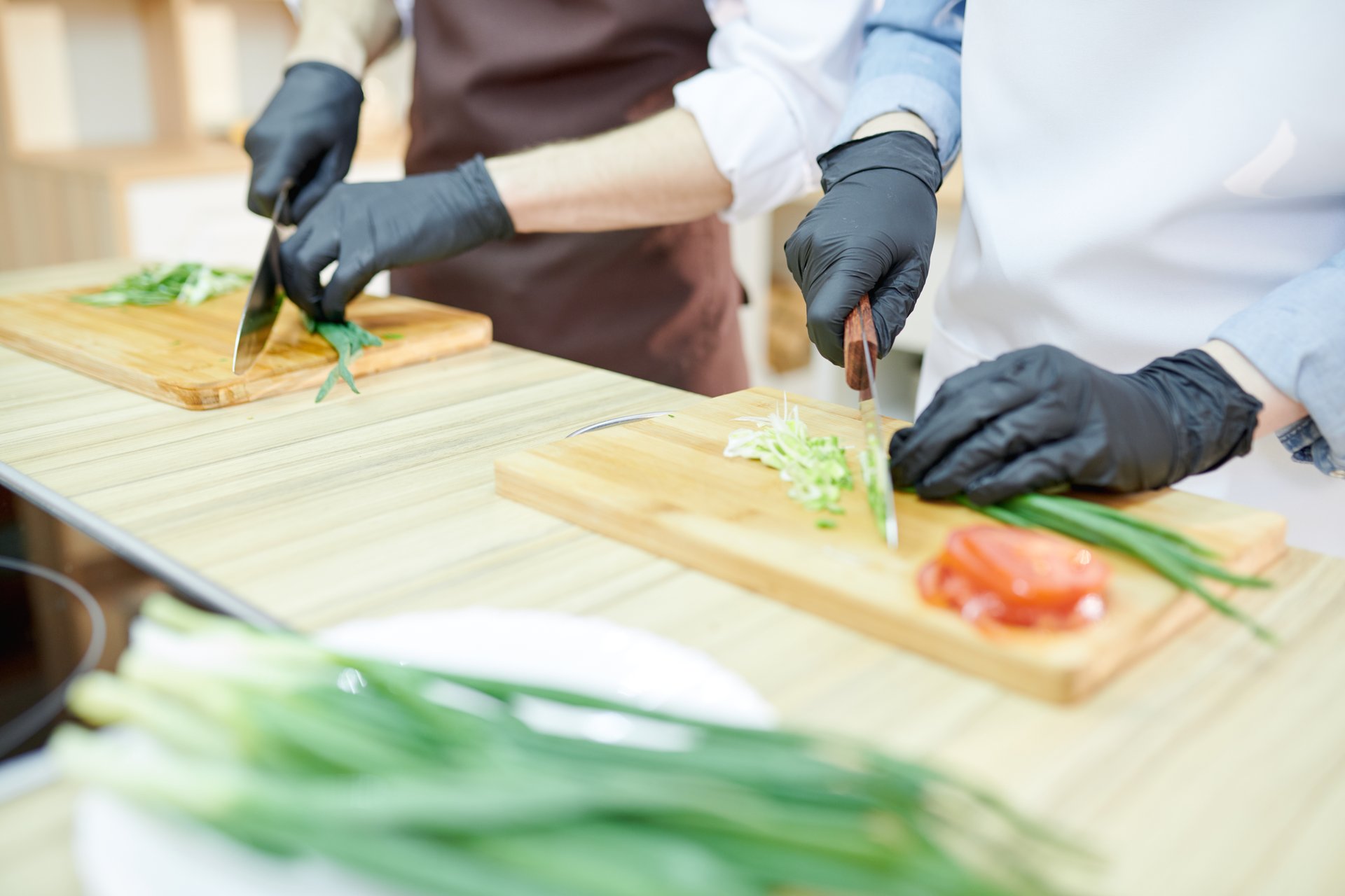 Cocinero cortando verduras frescas con guantes de nitrilo negros en cocina industrial.