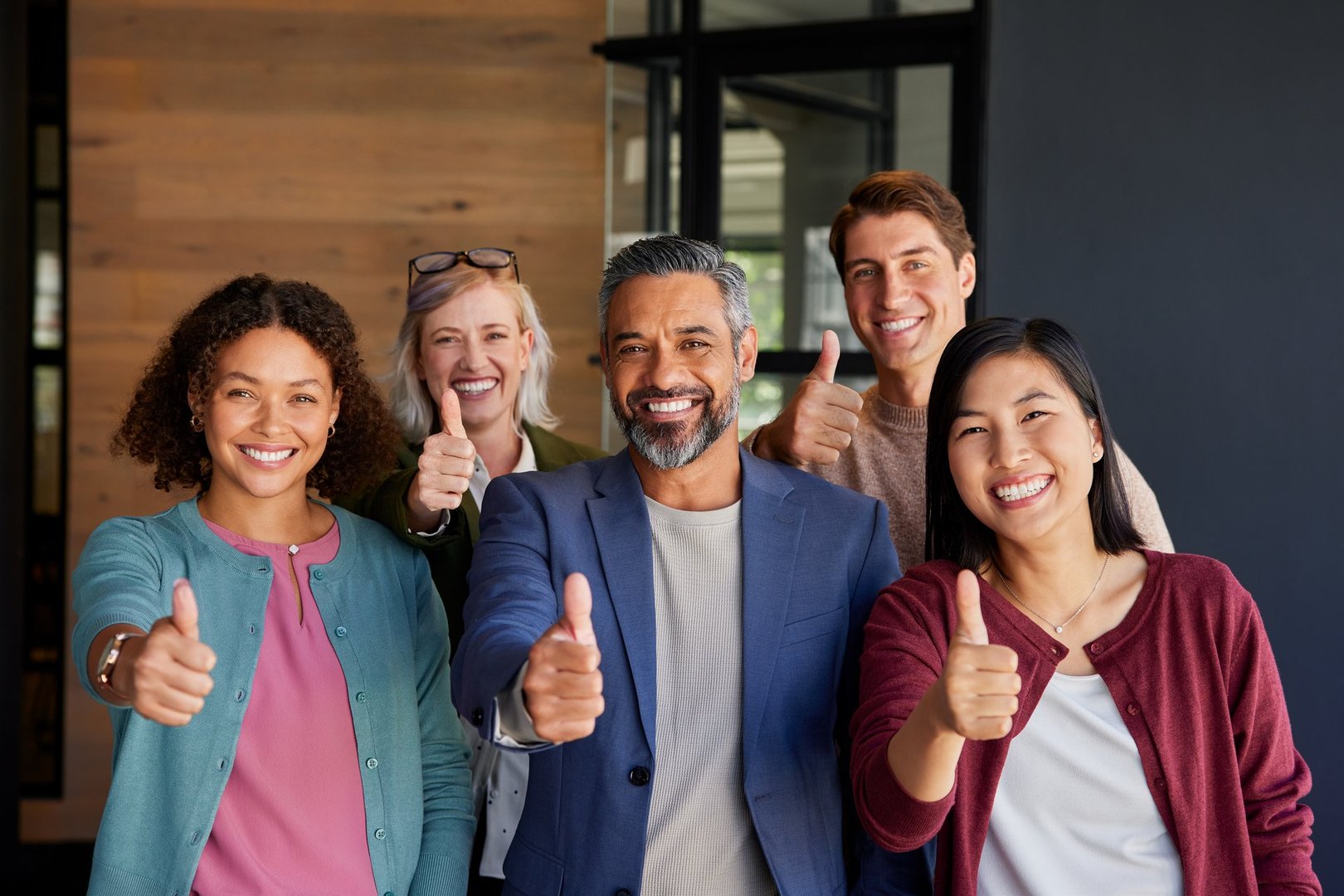 Group of multiethnic business people giving thumbs up, symbolizing success and positivity. Smiling business team showing approval and confidence in a modern office. Happy businesswomen and businessmen expressing support and encouragement with thumbs-up gestures.