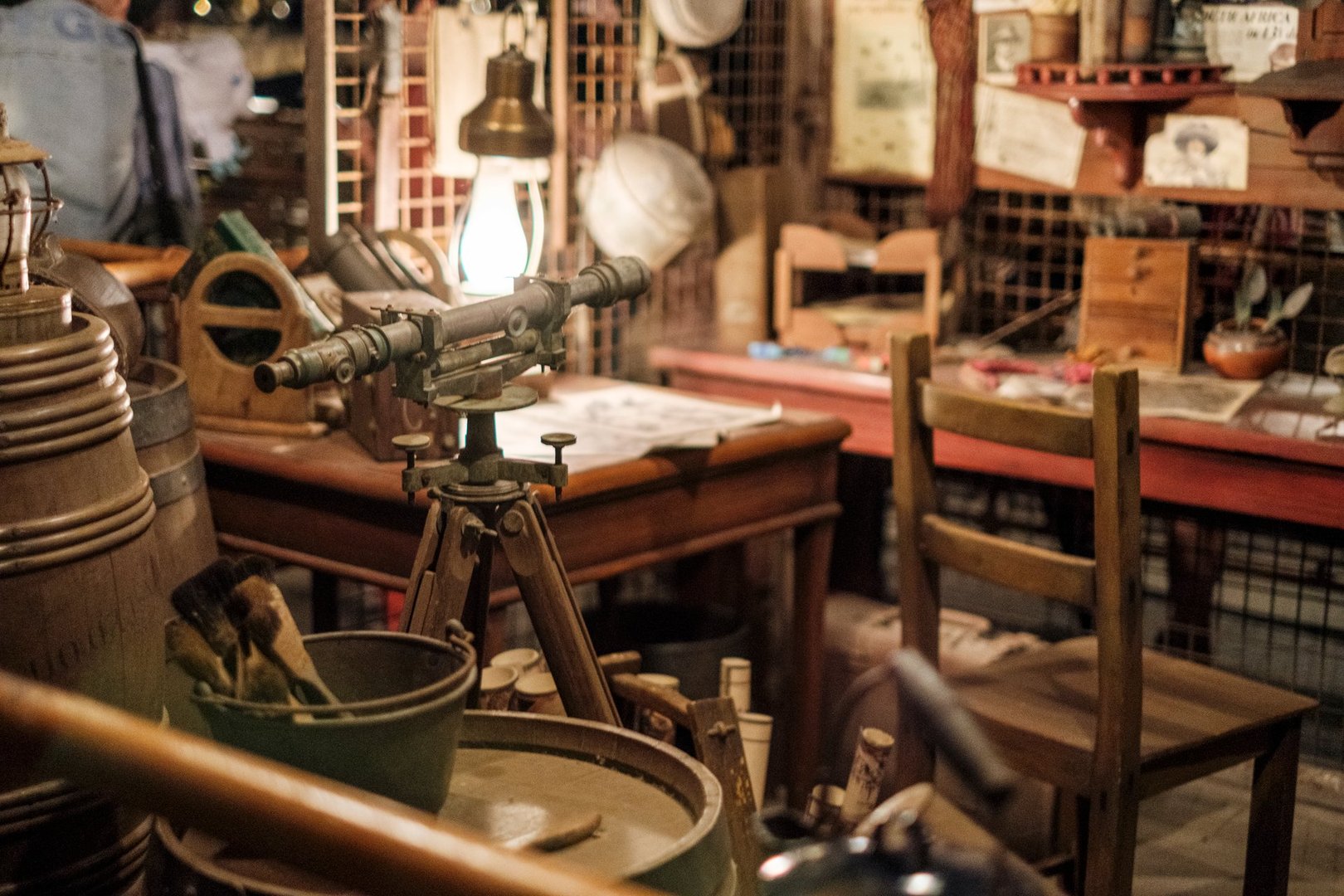 An antique shop showcases a rich collection of vintage items and historical artifacts. Visitors can explore various objects, from wooden barrels to old maps, under soft lighting.