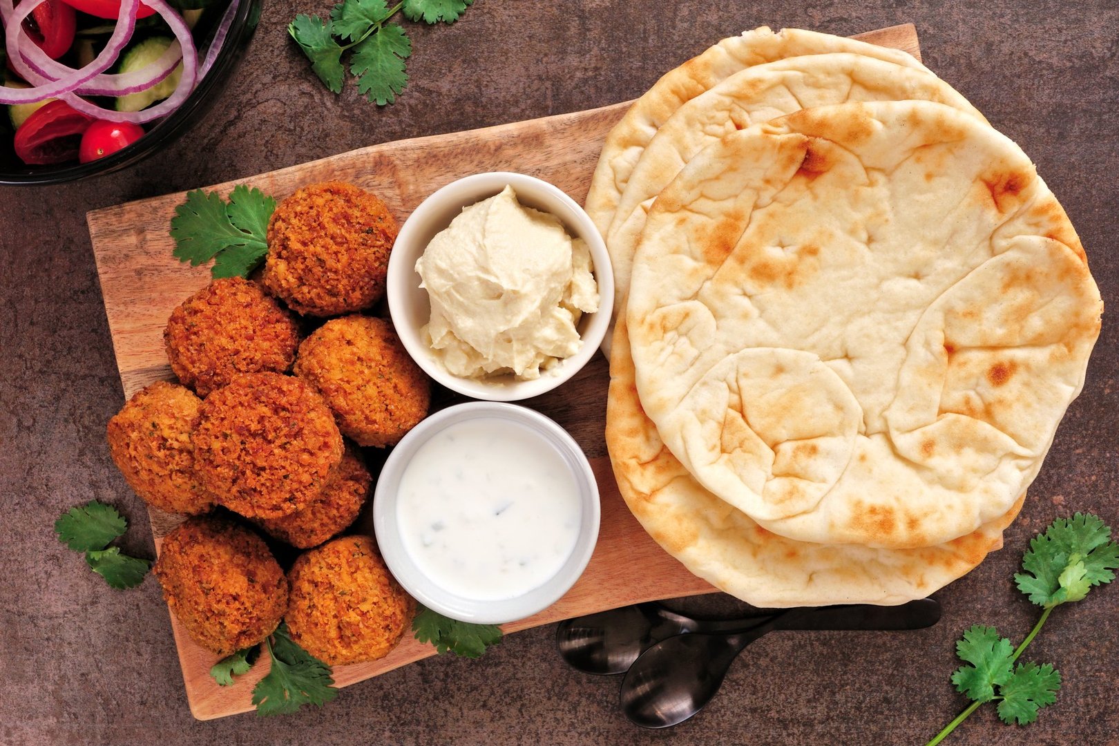 Vegetarian falafels and pita bread with tzatziki and hummus. Overhead view platter on a dark stone background.