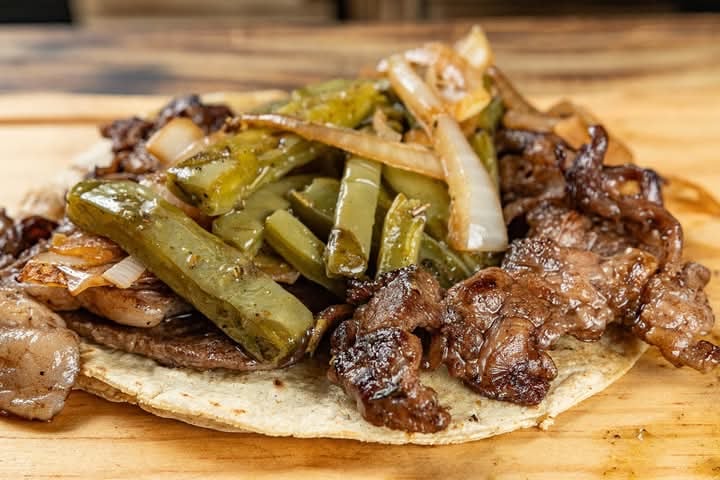 Taco with grilled steak, sliced cactus, and onions on a wooden surface.