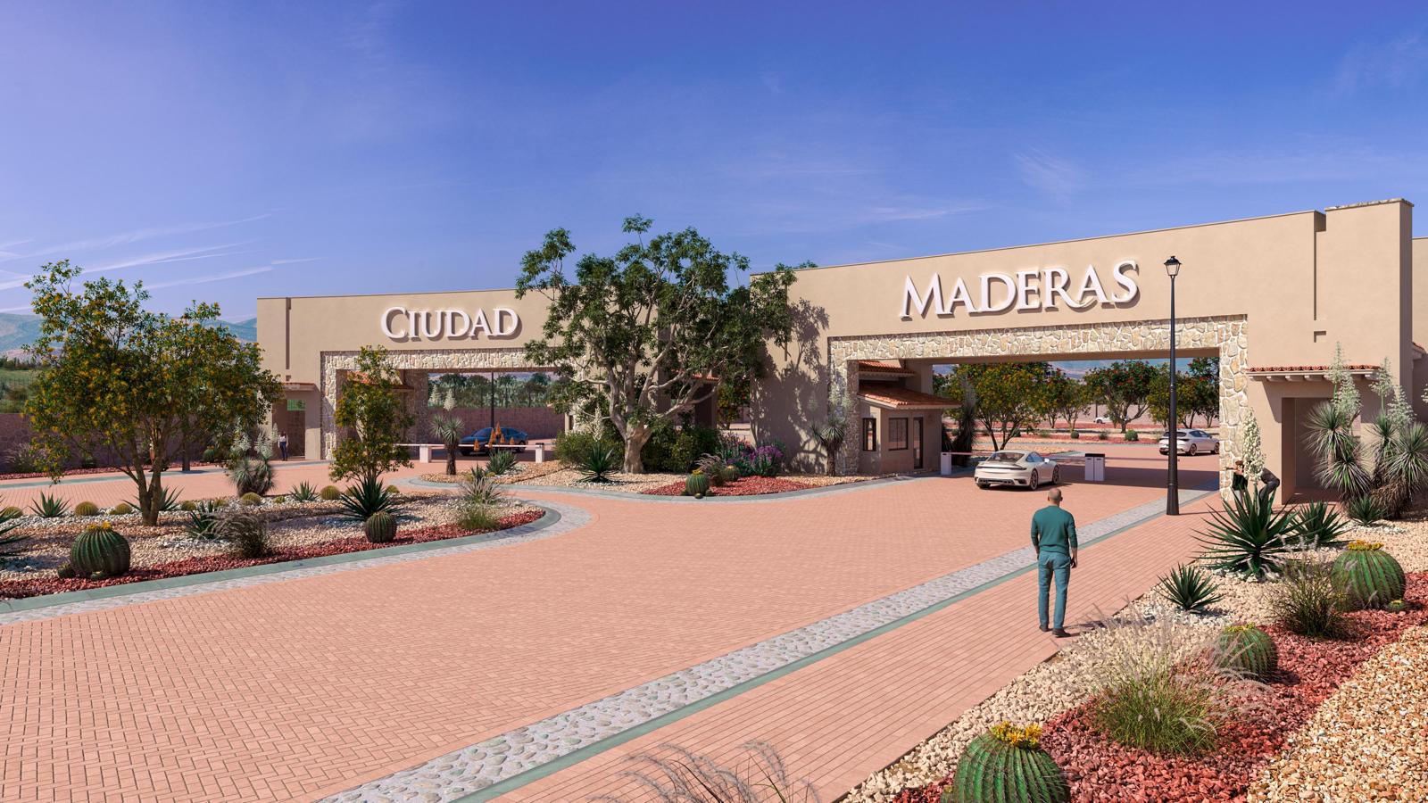 Entrance gate of Ciudad Maderas with a car and a person walking, surrounded by desert landscaping under a clear blue sky.