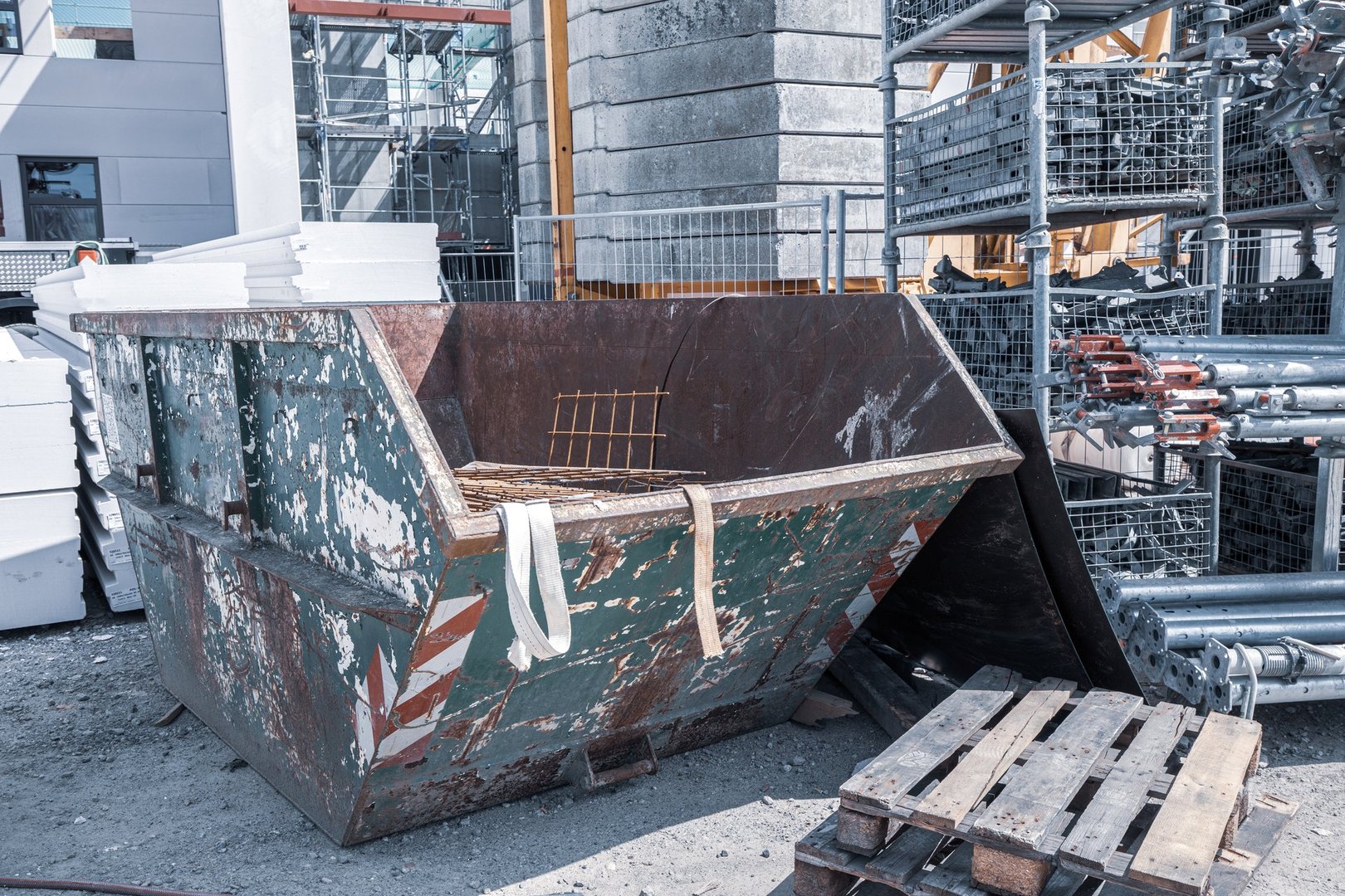 on a construction site, a waste container stands next to a shelf with scaffolding parts