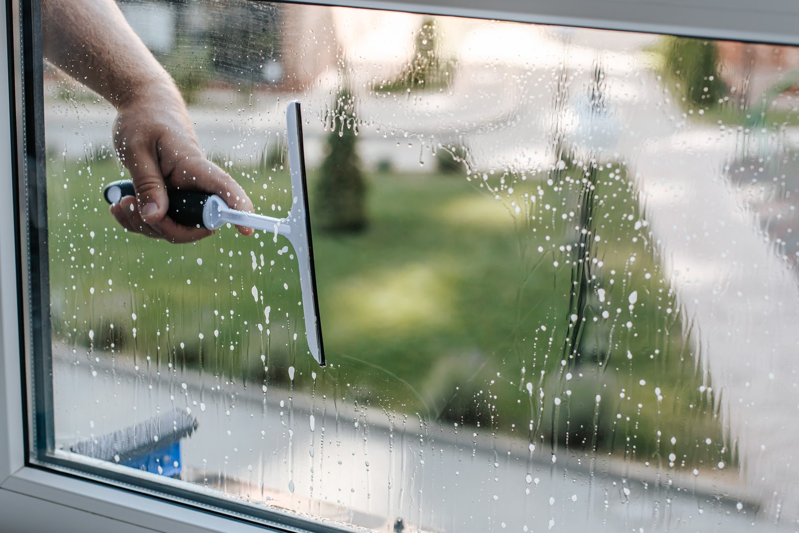 a man's hand with a window cleaning brush wipes foam from the window. against the backdrop of another house