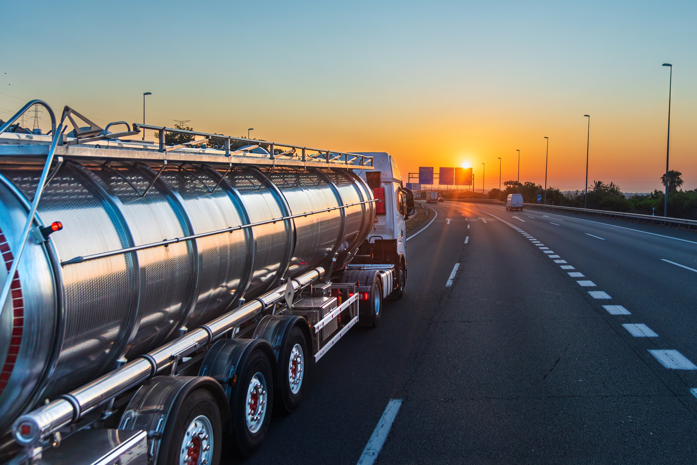 Tanker truck driving on a highway facing the rising sun at dawn.Side view.
