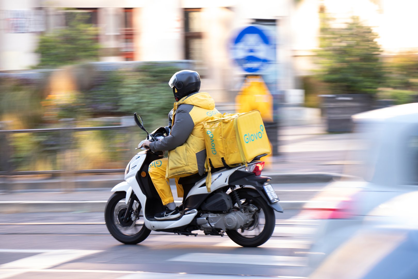 Belgrade, Serbia -  May 17, 2025: Glovo service courier with a delivery bag riding moto scooter in city street traffic