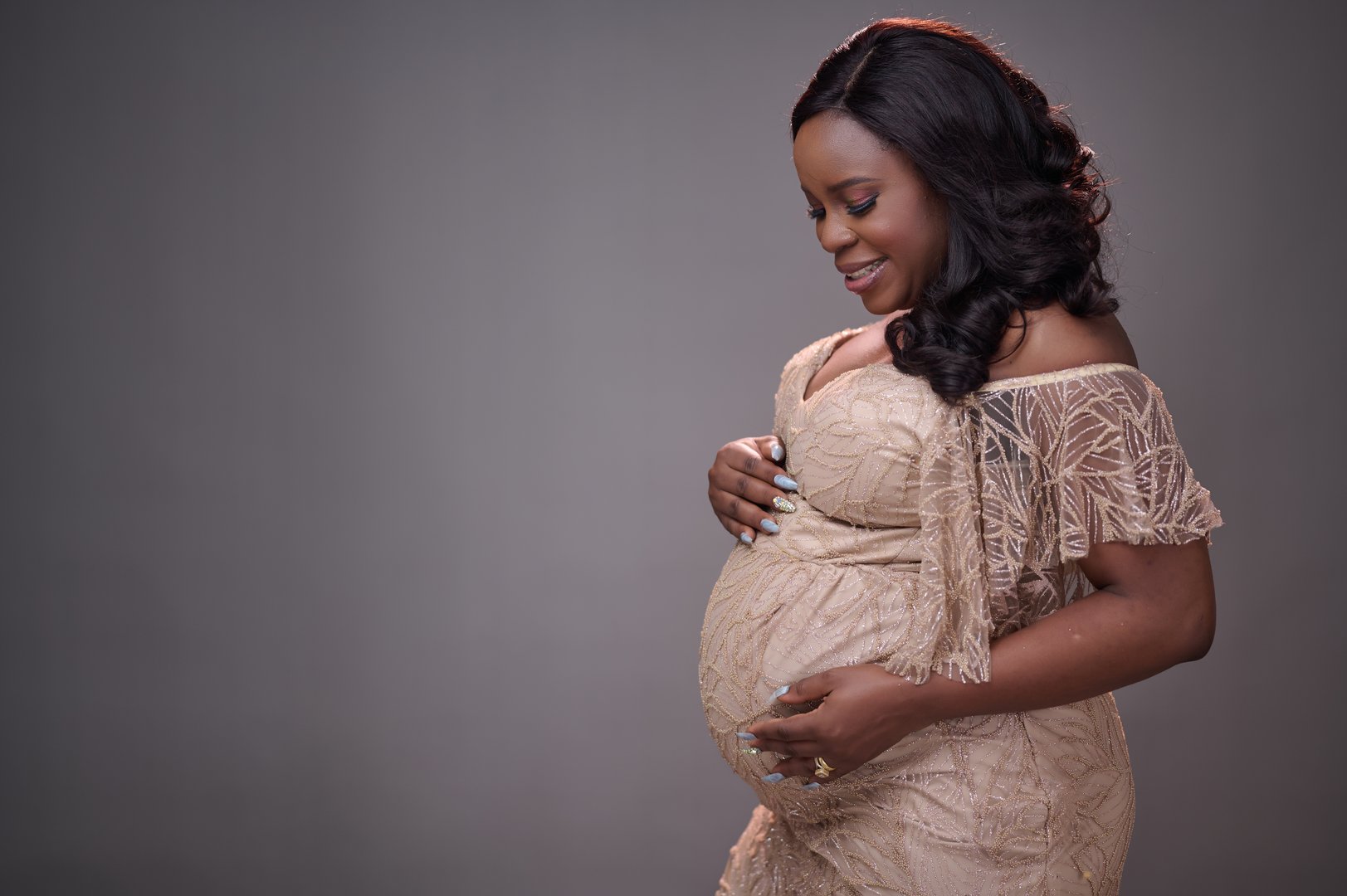 elegant maternity photoshoot featuring a glowing African mother-to-be dressed in a beautifully crafted, off-shoulder, gold lace gown.