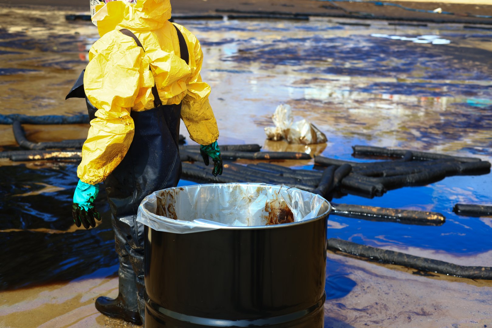 A person in a protective suit walking along a polluted shore and Clean up a Crude oil stain