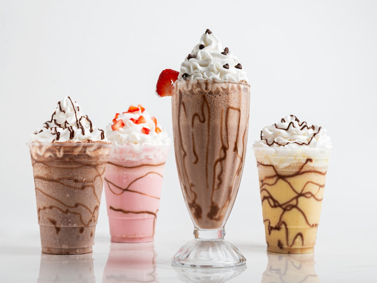 Four tempting milkshake variations: chocolate, strawberry, vanilla, and a mocha blend, each topped with whipped cream and chocolate drizzle