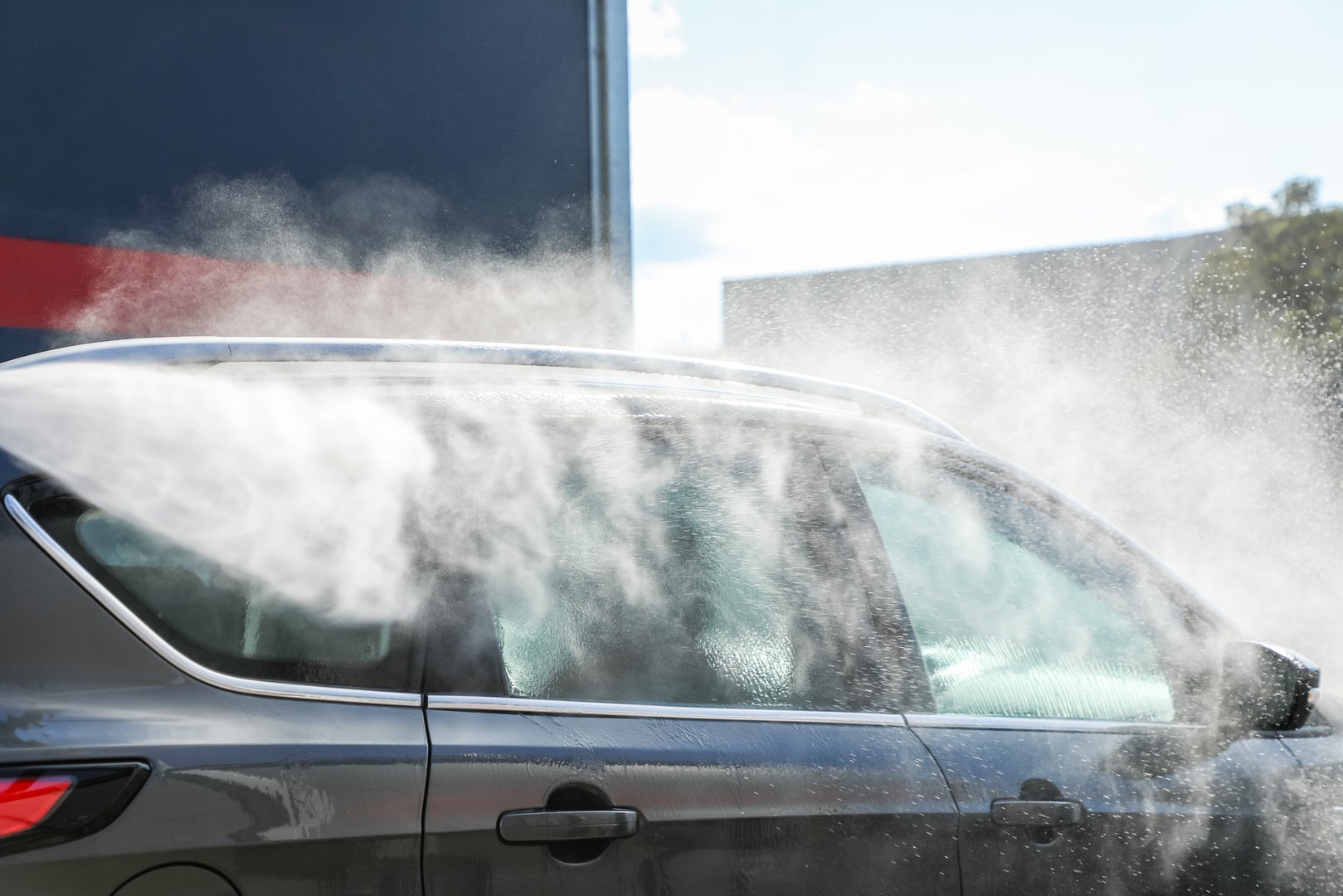 Car being thoroughly cleaned with a powerful high-pressure jet under radiant sunlight, highlighting gleaming surfaces and professional car care (part of the 
