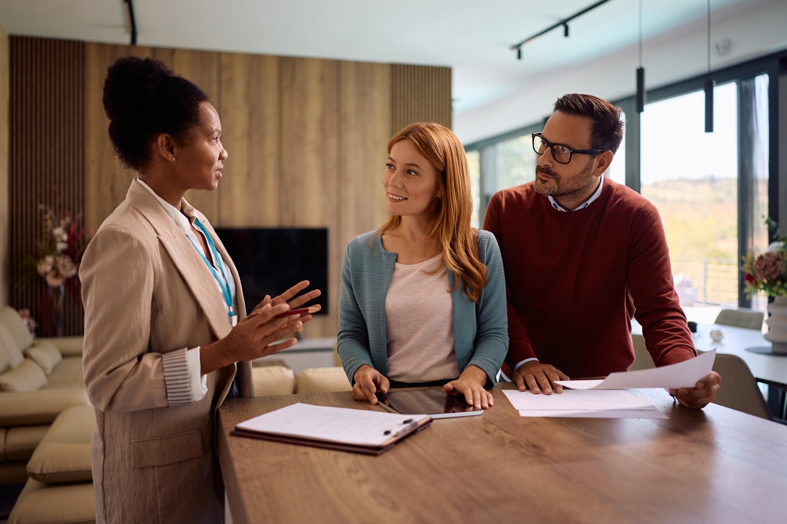 Happy woman and her husband analyzing housing plans while communicating with real estate agent.