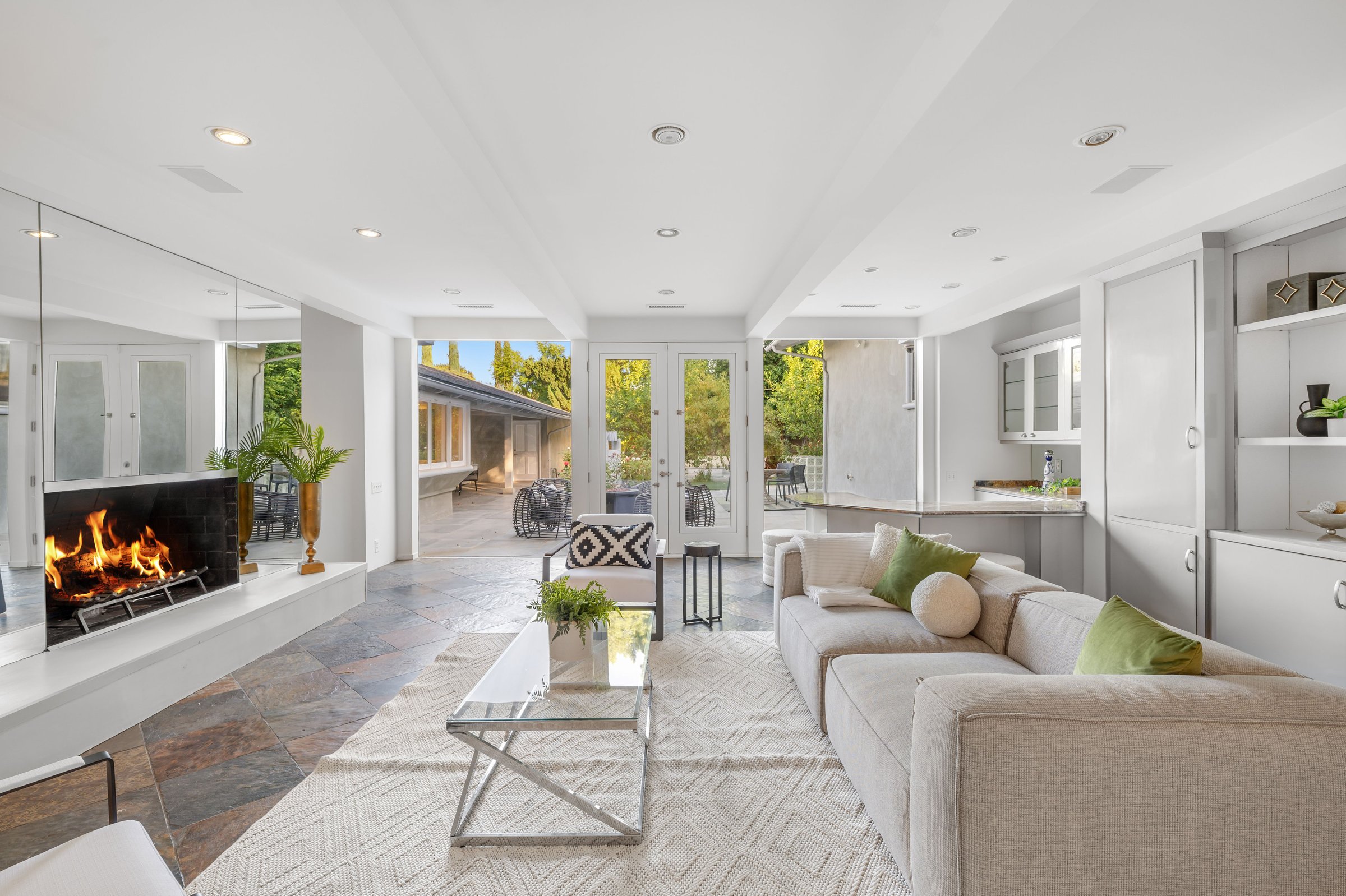 Modern living room with fireplace, beige sofa, and outdoor view through glass doors, creating a cozy and inviting atmosphere.