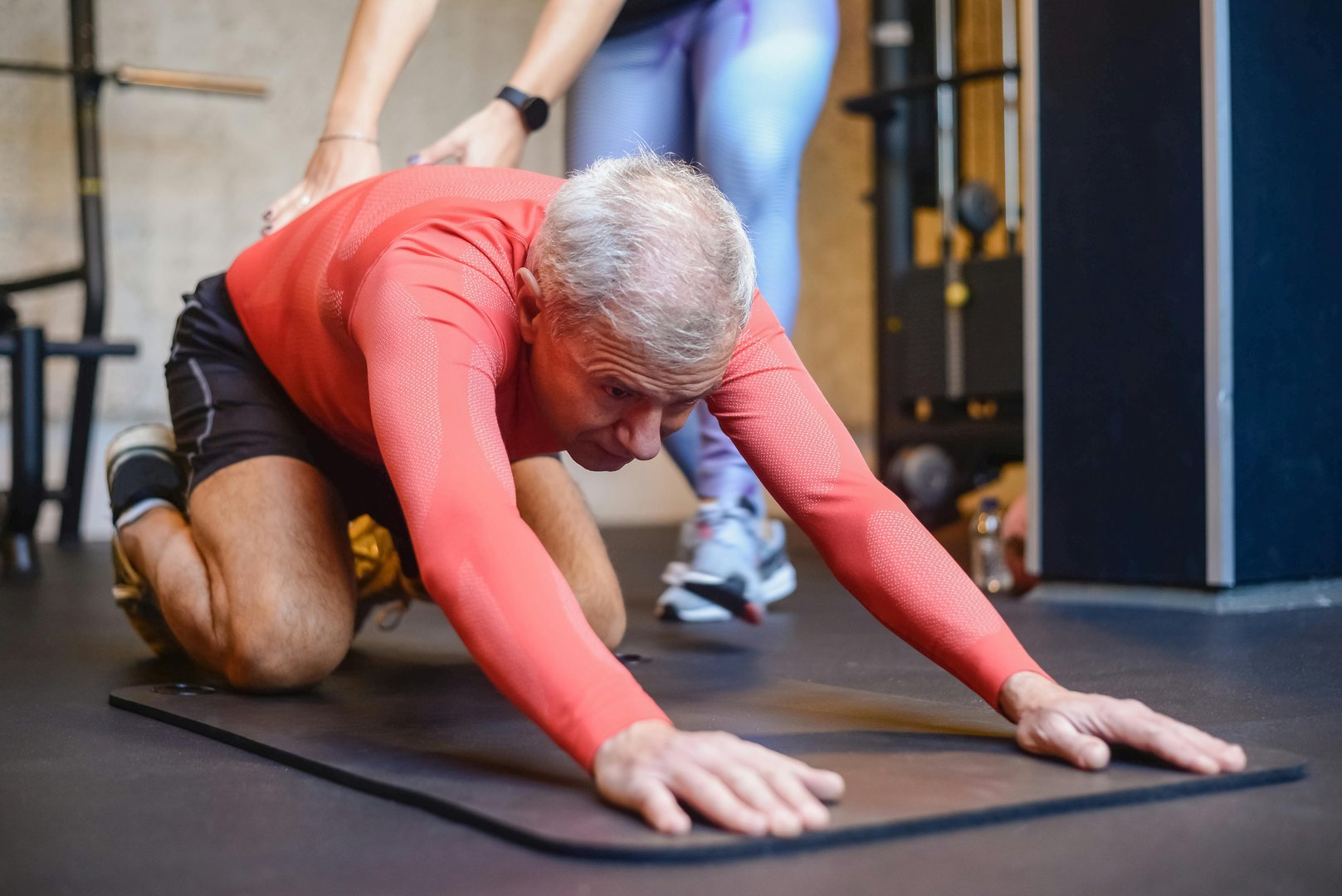 Pilates instructor guides her student through a challenging stretching exercise on a reformer machine in a modern pilates studio