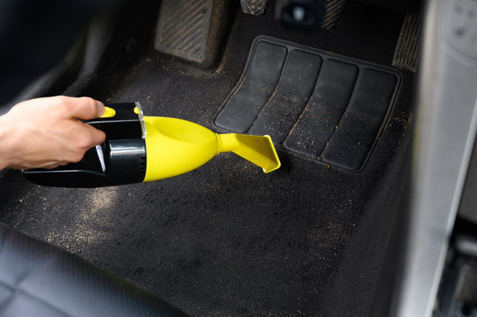 Car interior cleaning, close-up. Man vacuuming floor in car cabin with portable vacuum cleaner. Professional cleaning of car upholstery, carpet. Maintaining cleanliness in car.