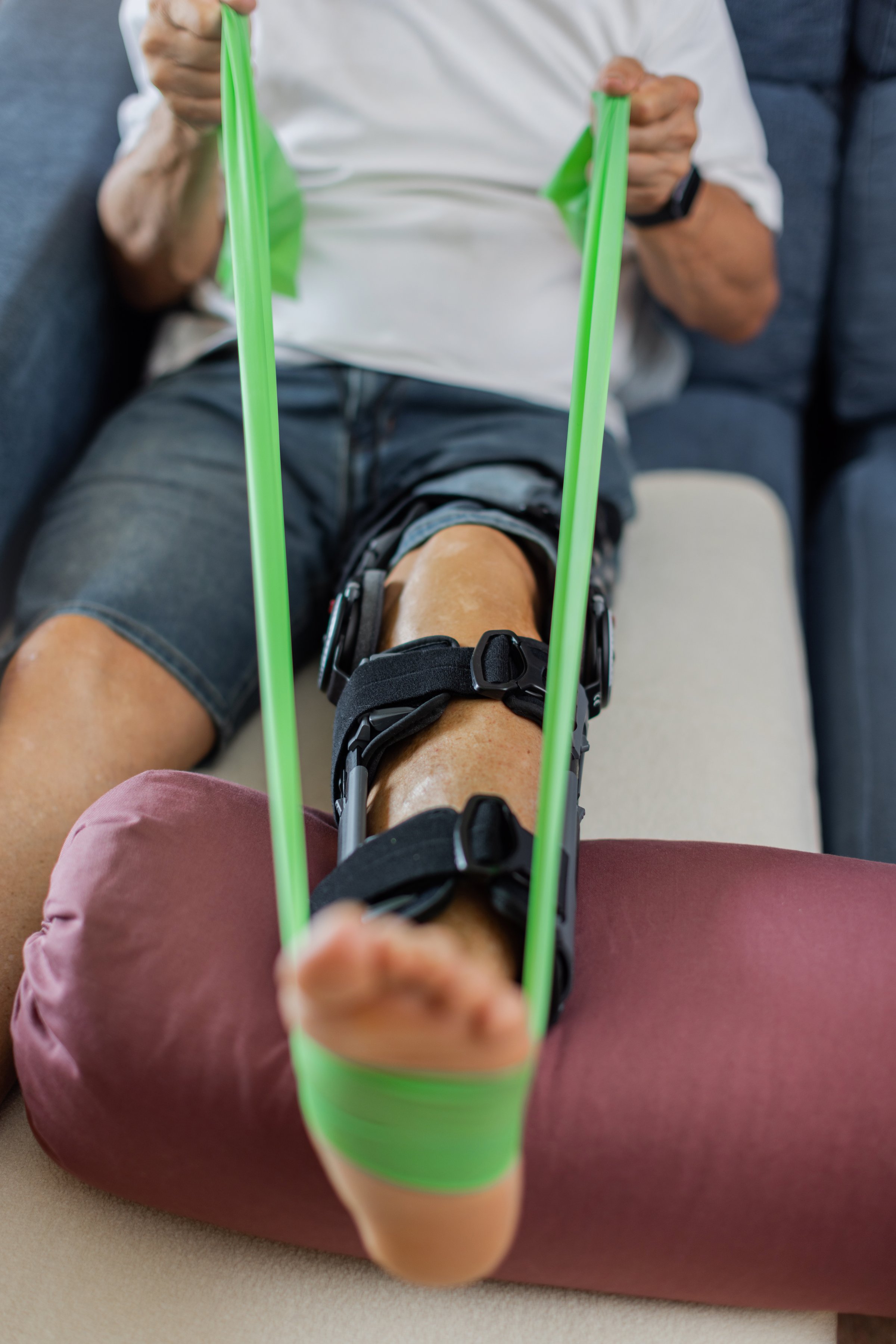 Part of Senior Man performing rehabilitation exercises using resistance equipment to aid in his knee recovery process. A Physical Therapy Exercise with leg brace. Unrecognizable, cropped. vertical.