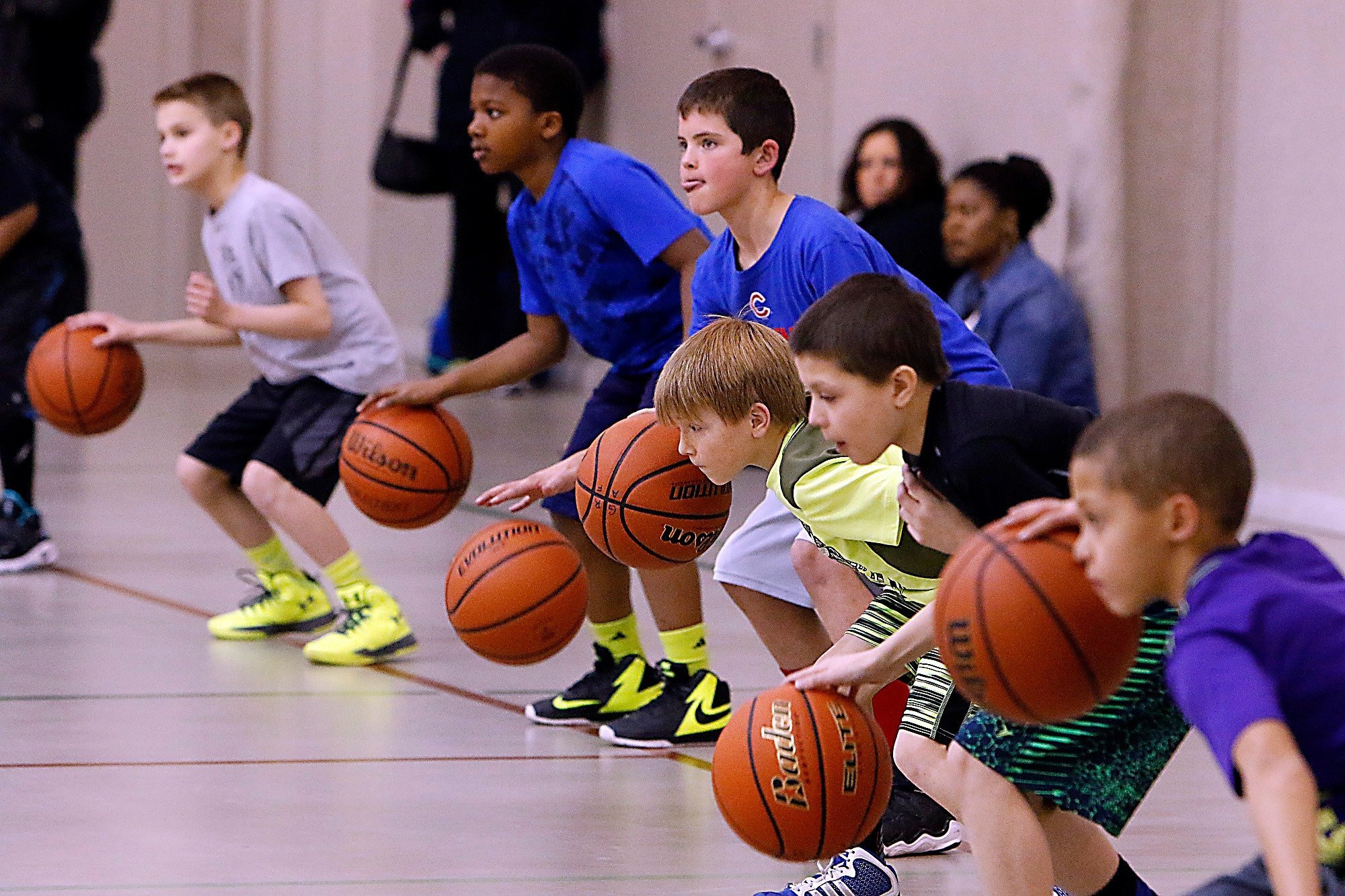 Young boys practicing basketball dribbling in a gym, each with a basketball, focused on their skills.
