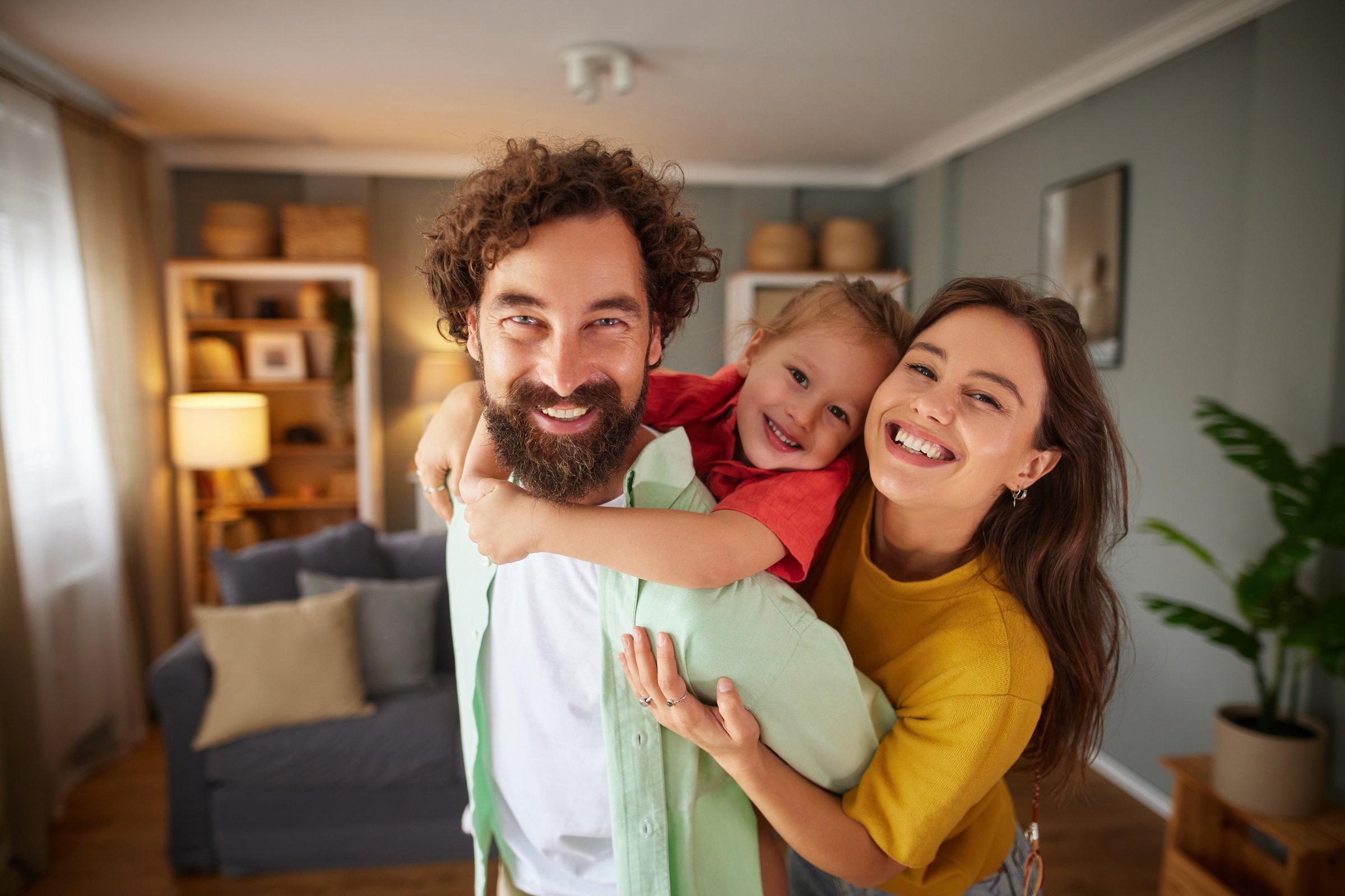 Family of three laughing and hugging, enjoying time together in a domestic setting