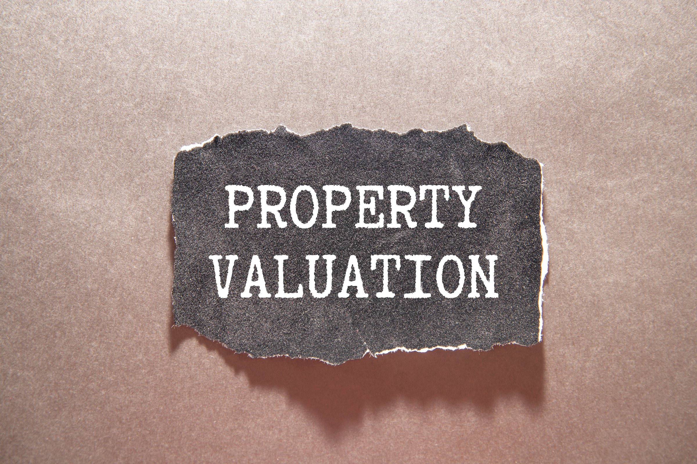 Property valuation text on notepad with house model and key on wooden desk