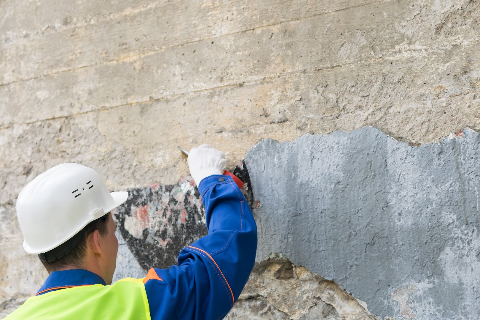 a man in a helmet clears a wall of forbidden inscriptions, view from the back