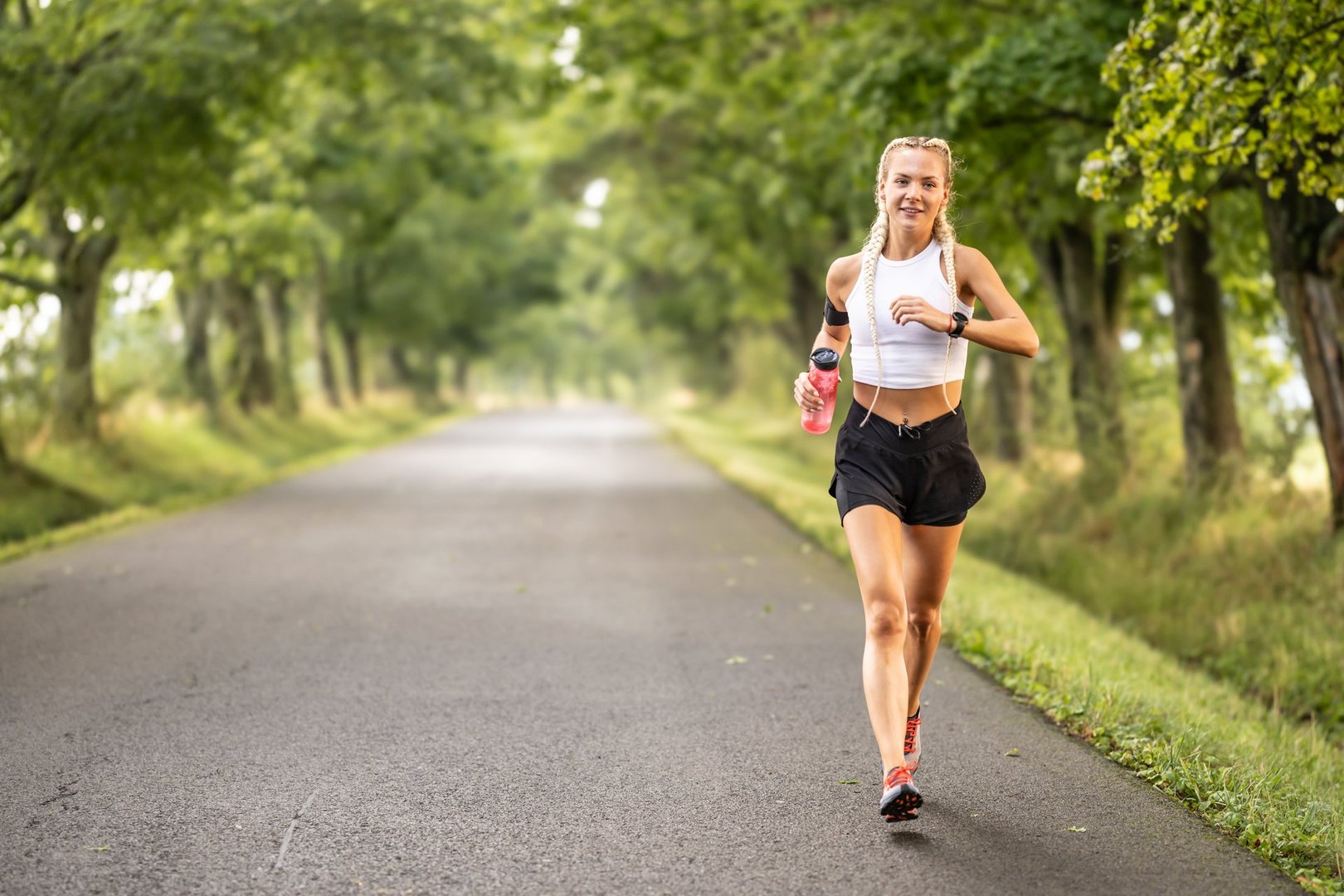 Female runner jogging outside in the park. Young woman runner running with a bottle of water.