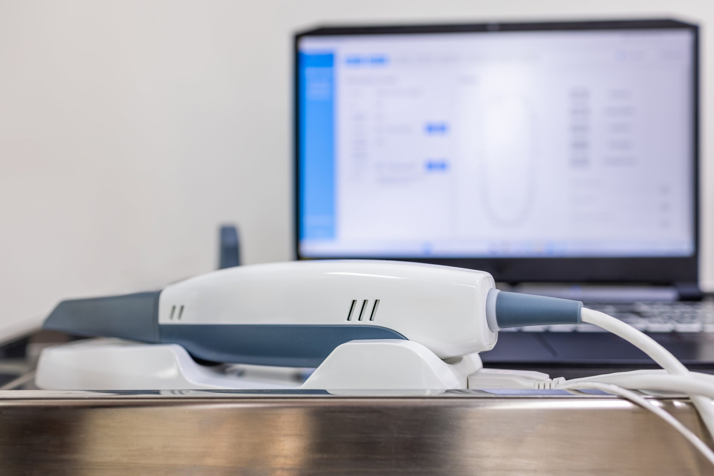 Intraoral scanner with connected software system in the background, used for creating accurate 3D dental impressions for restorative treatments