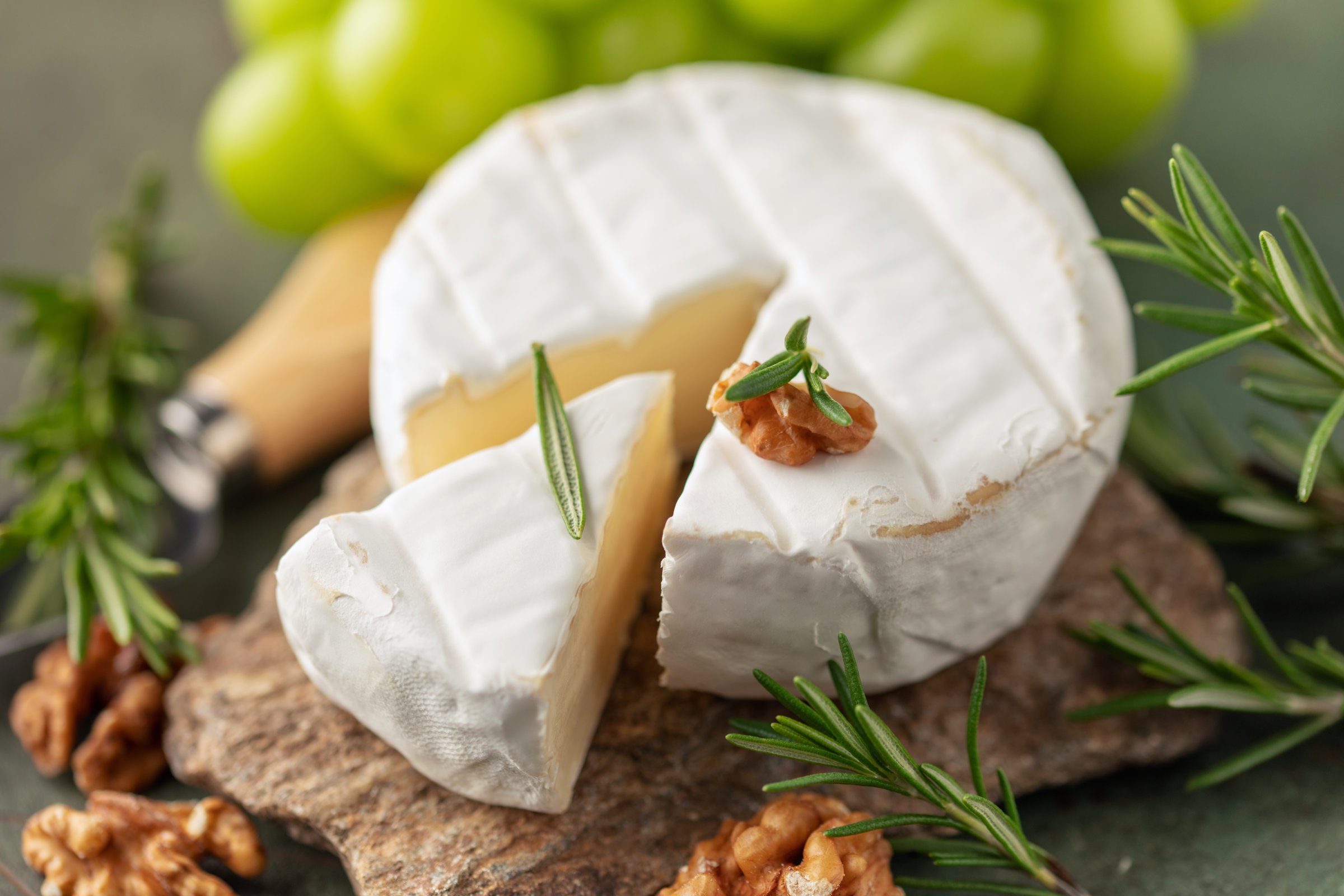 Soft brie or camembert cheese on a stone board, chine muscat grapes, walnut and rosemary branches on a green background