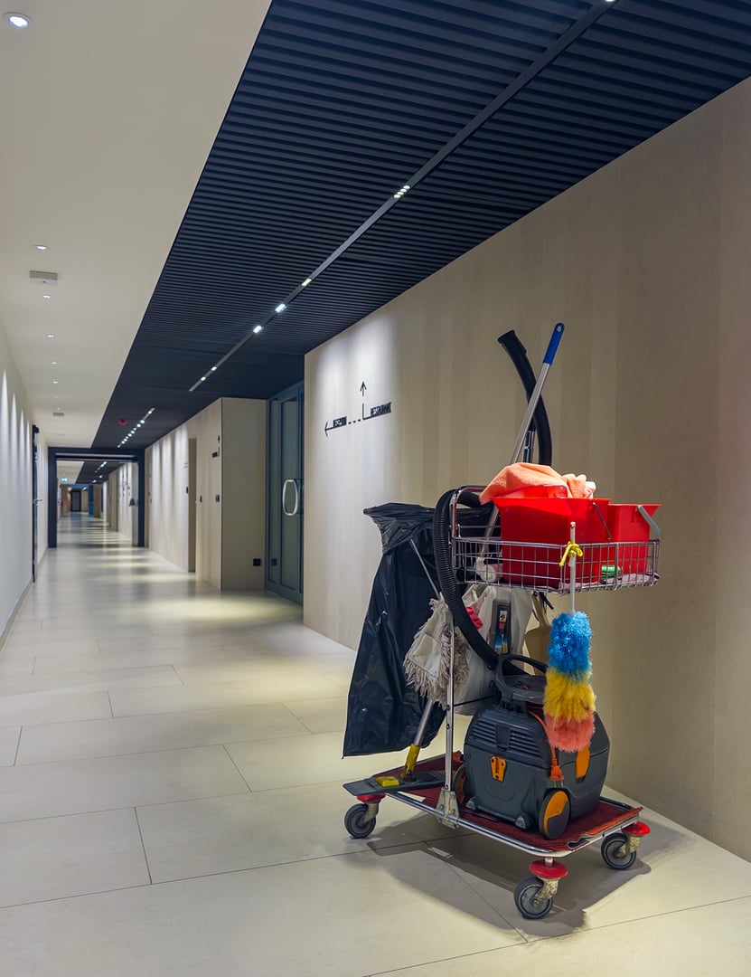 Cleaning cart with supplies in a modern office hallway, representing facility maintenance and commercial janitorial service in business environment.