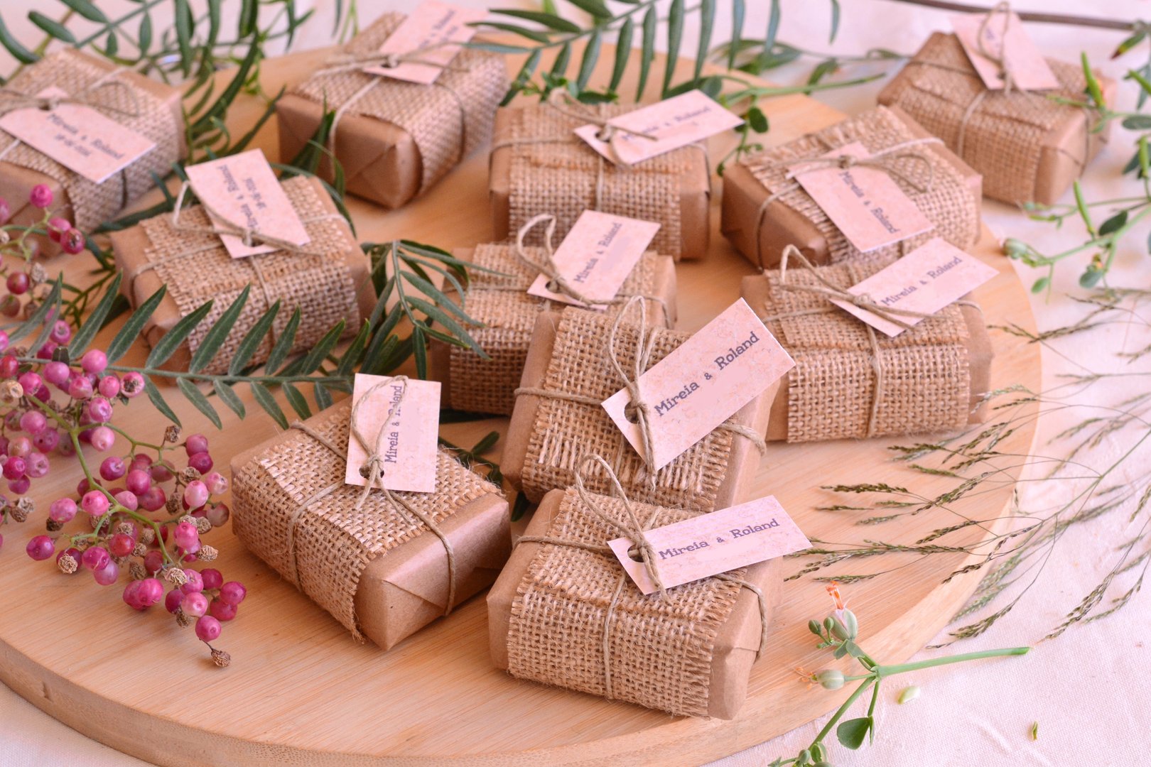 Autumn fall wedding decoration guest gifts favors rustic style soap boxes wrapped in brown craft paper jute fabric, ribbon and custom labels with names, wodden table background with red berries and green leaves
