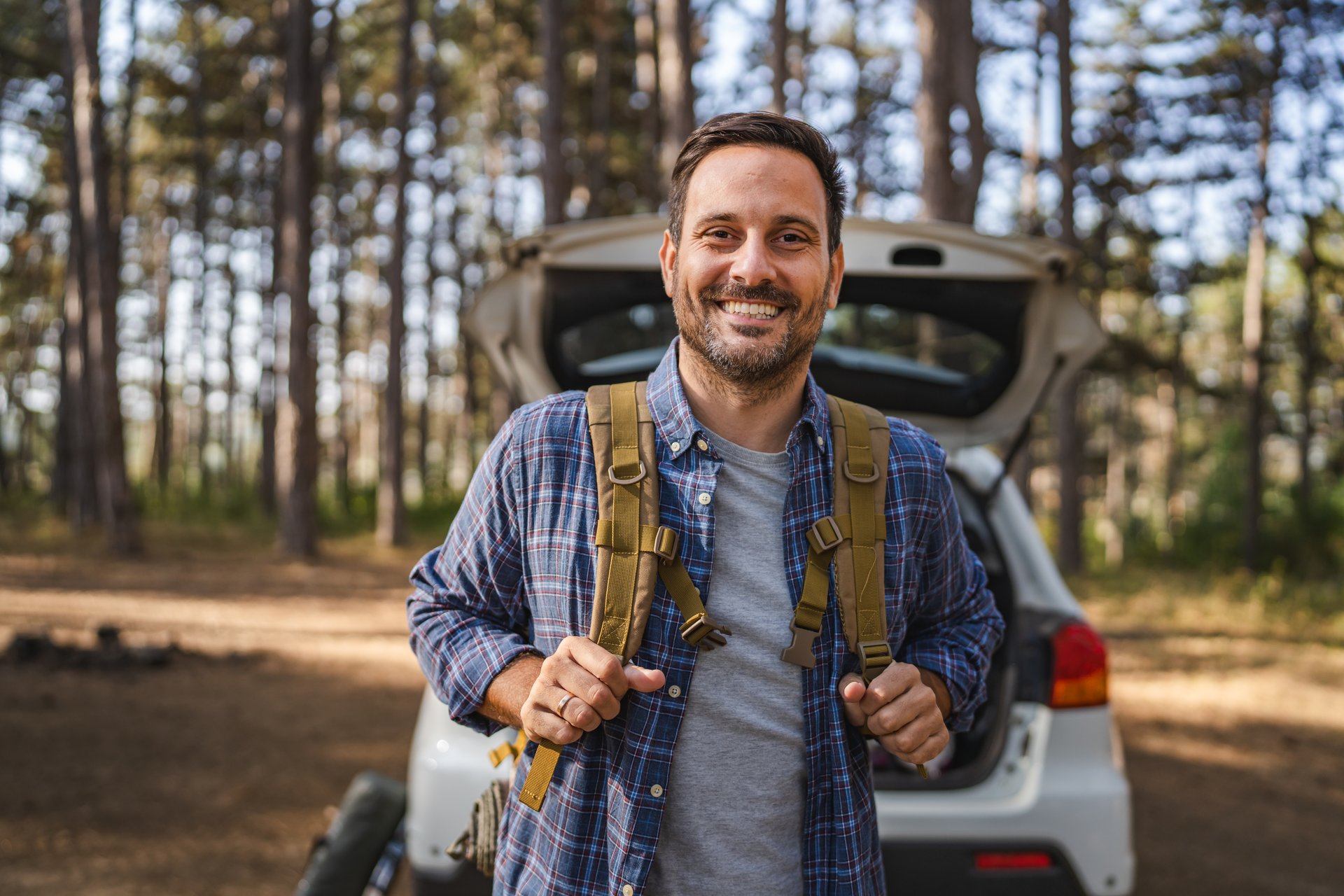Portrait of adult man camper hold backpack in front car in the forest