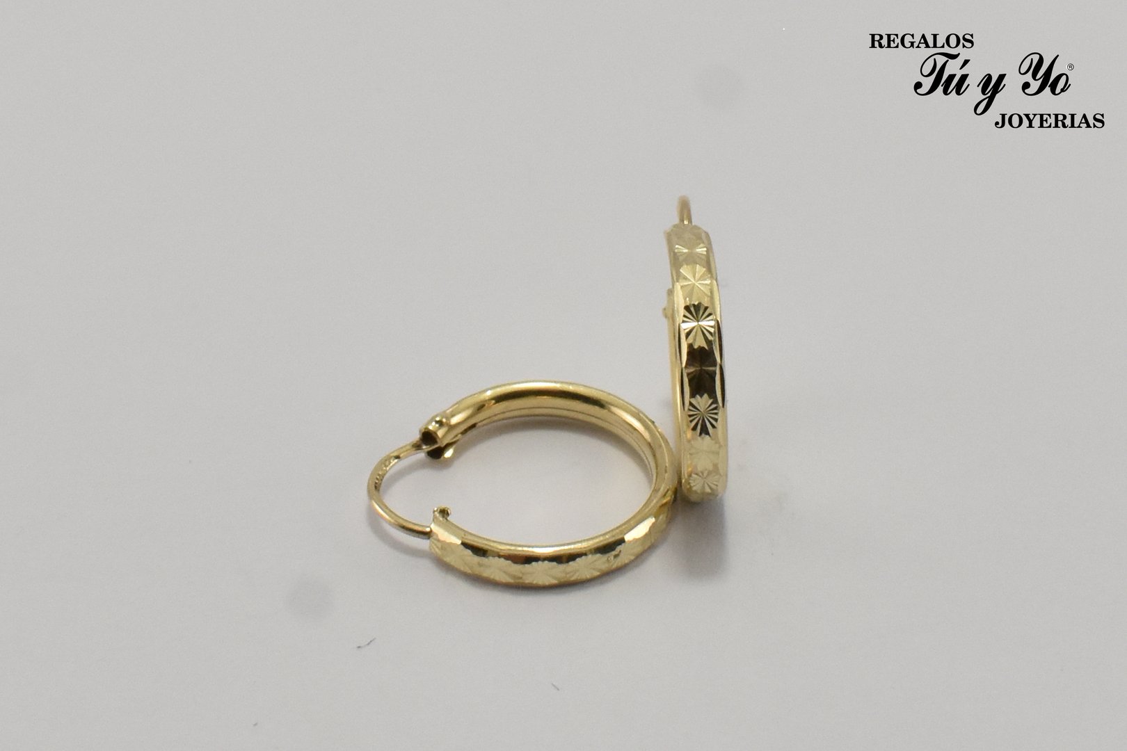 Gold hoop earrings with engraved star patterns, displayed against a white background. Branding in top right corner.