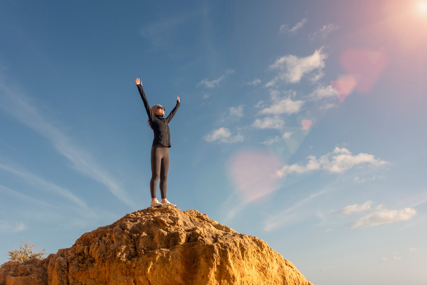 sporty woman standing on top of a cliif with her arms raised
