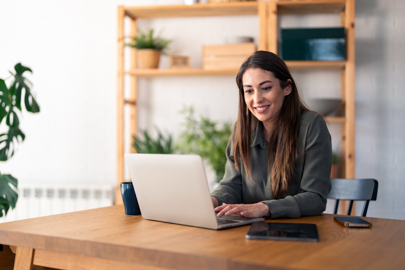 Satisfied beautiful millennial woman typing on laptop computer while sitting at table in home office.