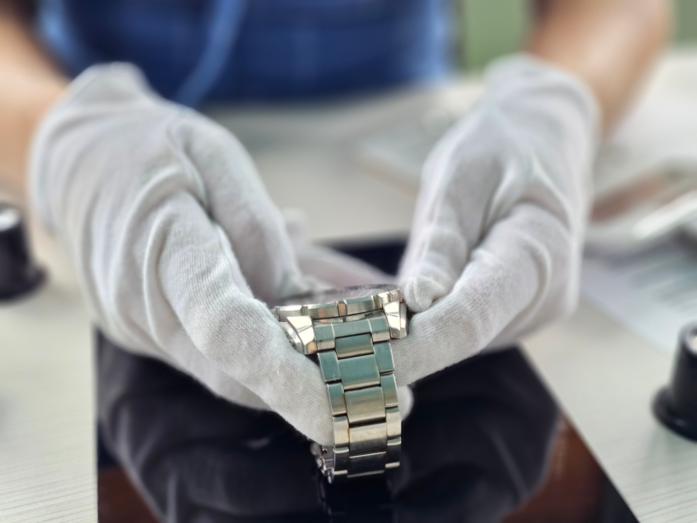 Watch repair technician adjusting a metal watch bracelet while using a tablet in a workshop setting