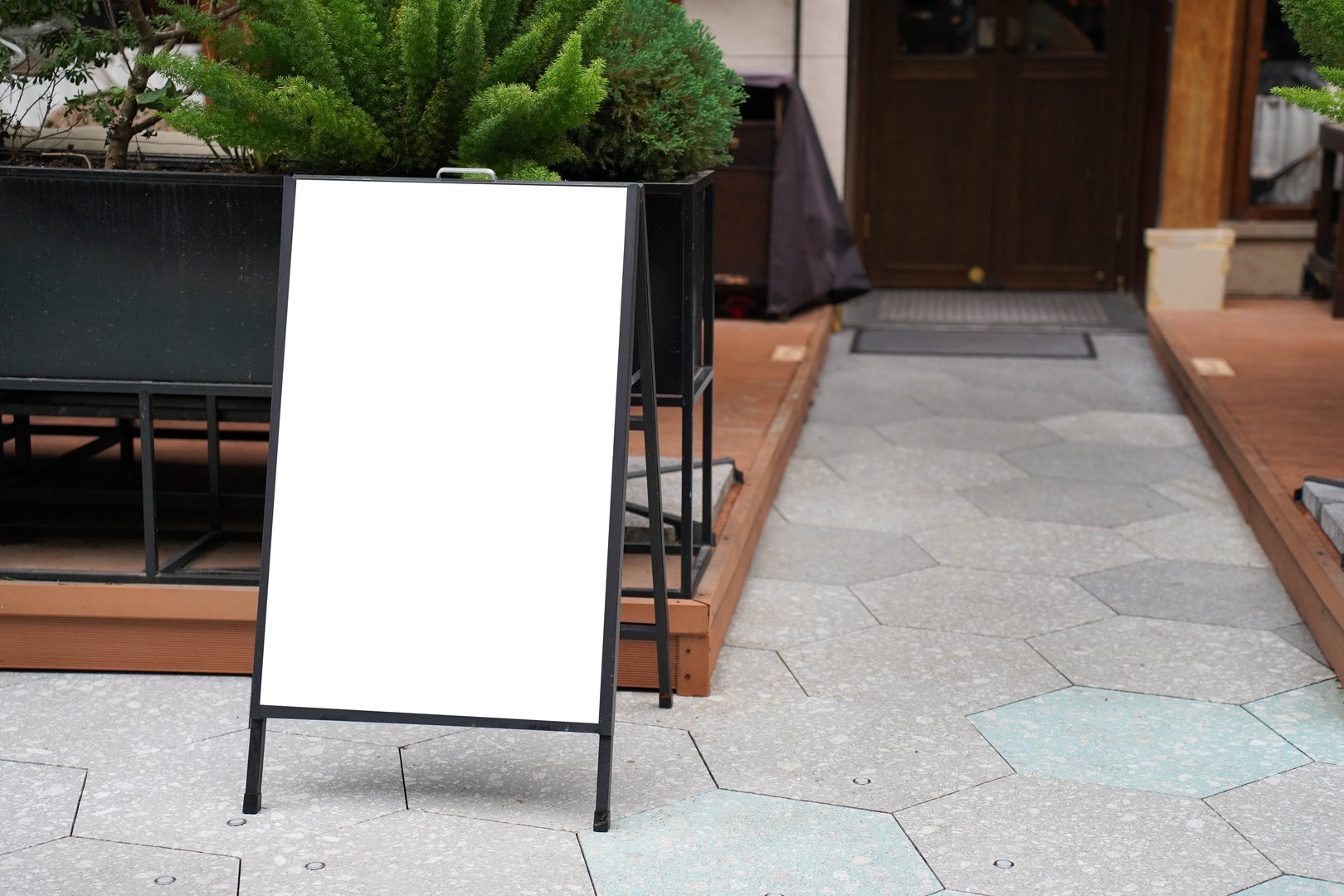 Blank white outdoor advertising stand sandwich board mock up template. Clear street signage board placed by an outdoor dinning area of a restaurant.