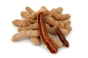 Cluster of tamarind pods with some peeled to reveal the brown pulp inside, arranged on a white background.