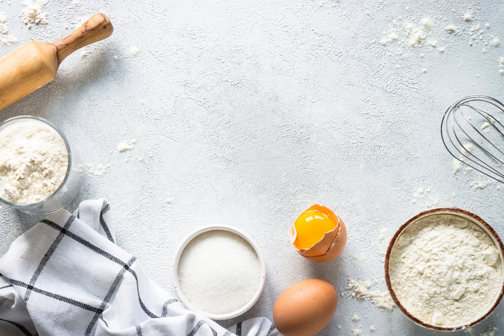 Baking background ingredients. Flour, sugar, eggs and rolling pin at light stone table. Top view with copy space.