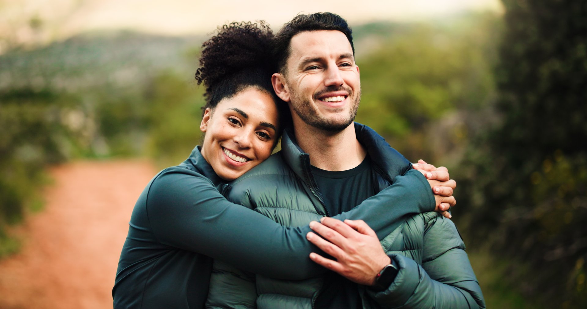Happy, hug and hiking with couple in nature for fitness, trekking adventure or love. Workout partner, hiker date and bonding with portrait of woman and man on path for health, vacation and connection