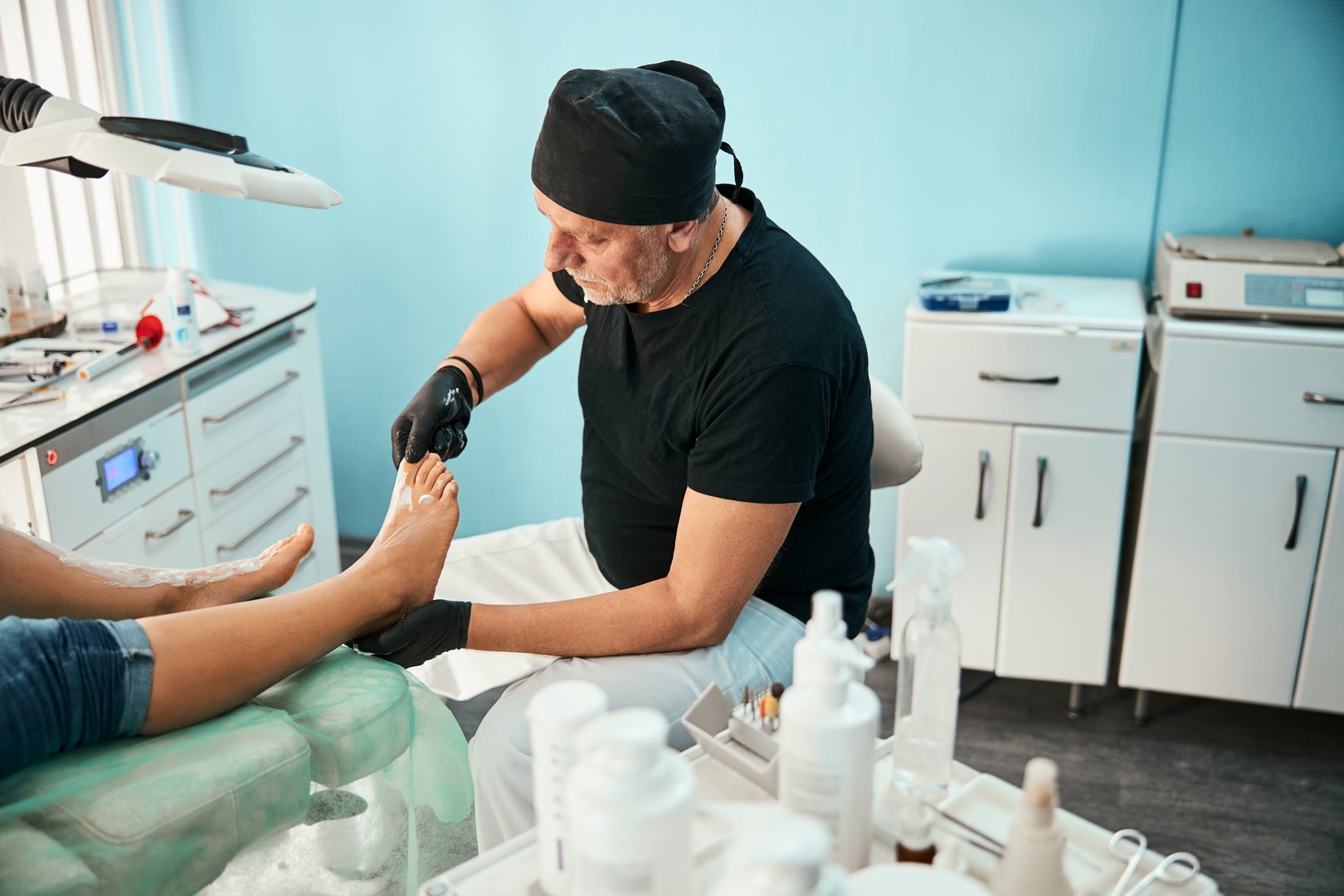 Podólogo realizando tratamiento a cliente usando guantes de nitrilo en espacio clínico.