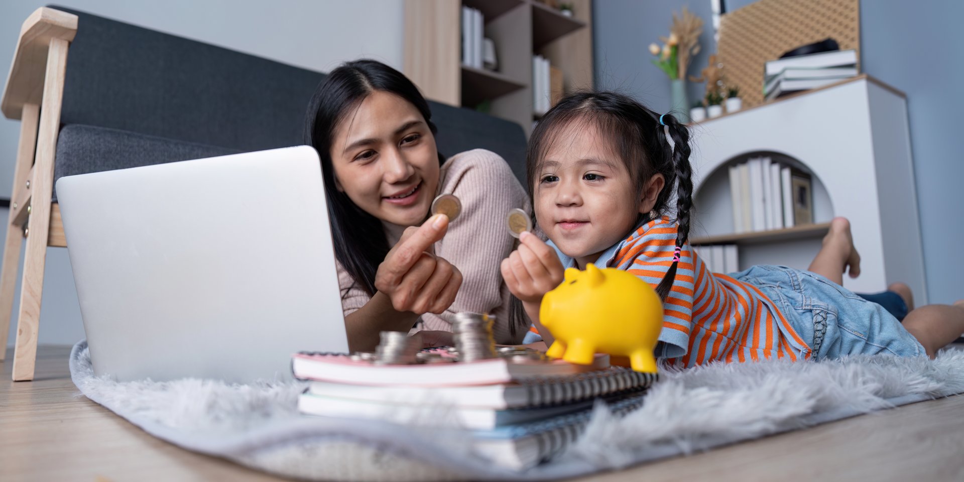 A mother uses coins and a piggy bank to teach her daughter about financial education, emphasizing saving money and economic literacy.