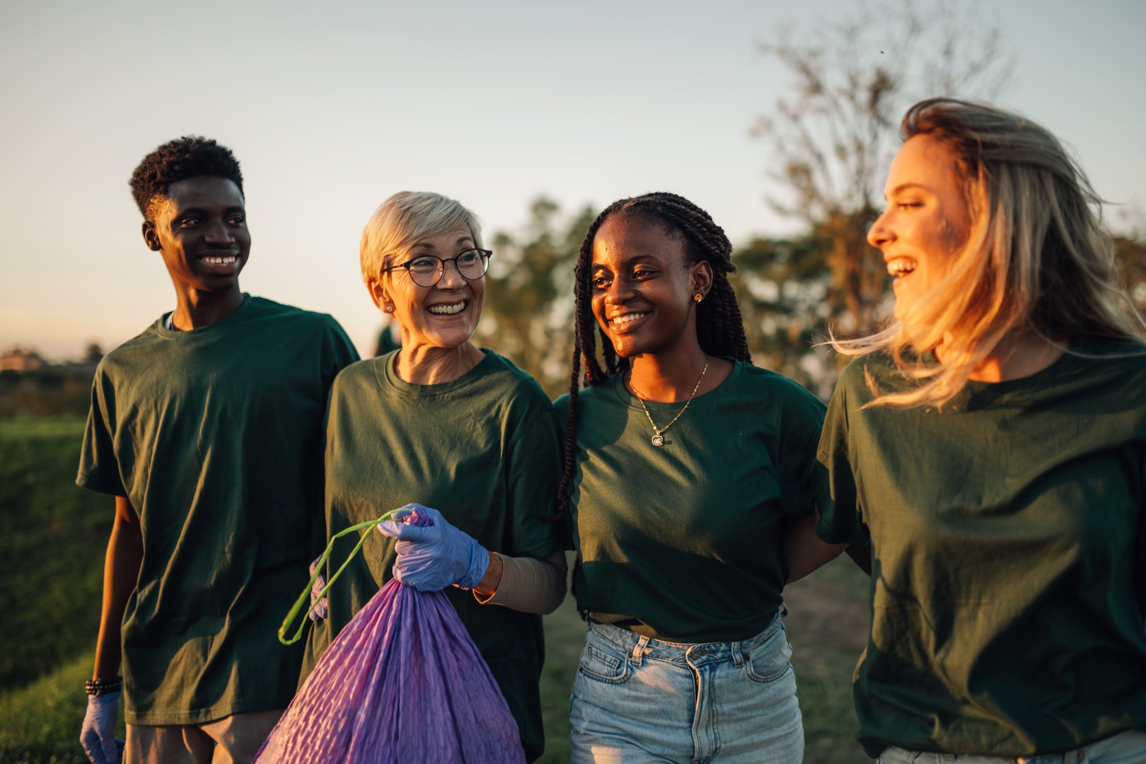 Volunteers are walking together outdoors and holding a garbage bag, they are smiling and happy to contribute to environmental protection