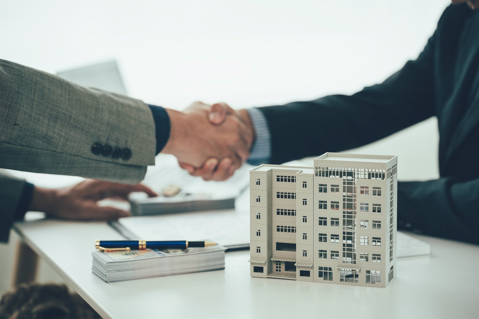 Two businessmen holding hands at the table represents a successful real estate deal. Close up of handshake between real estate agent and new home owner. Close-up photo.