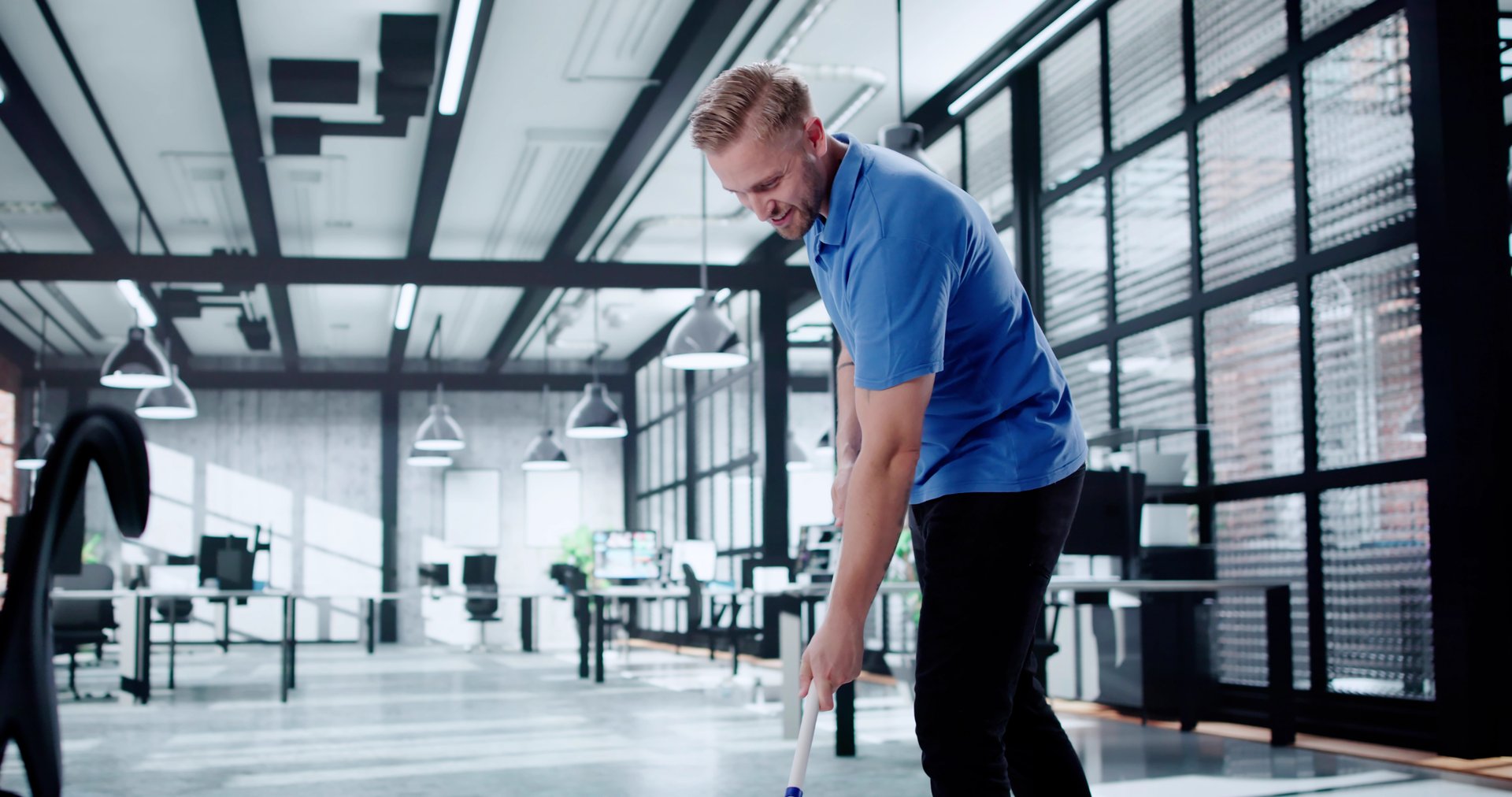 Smiling Cleaner In Blue Overalls Mopping Office Floor With Mop