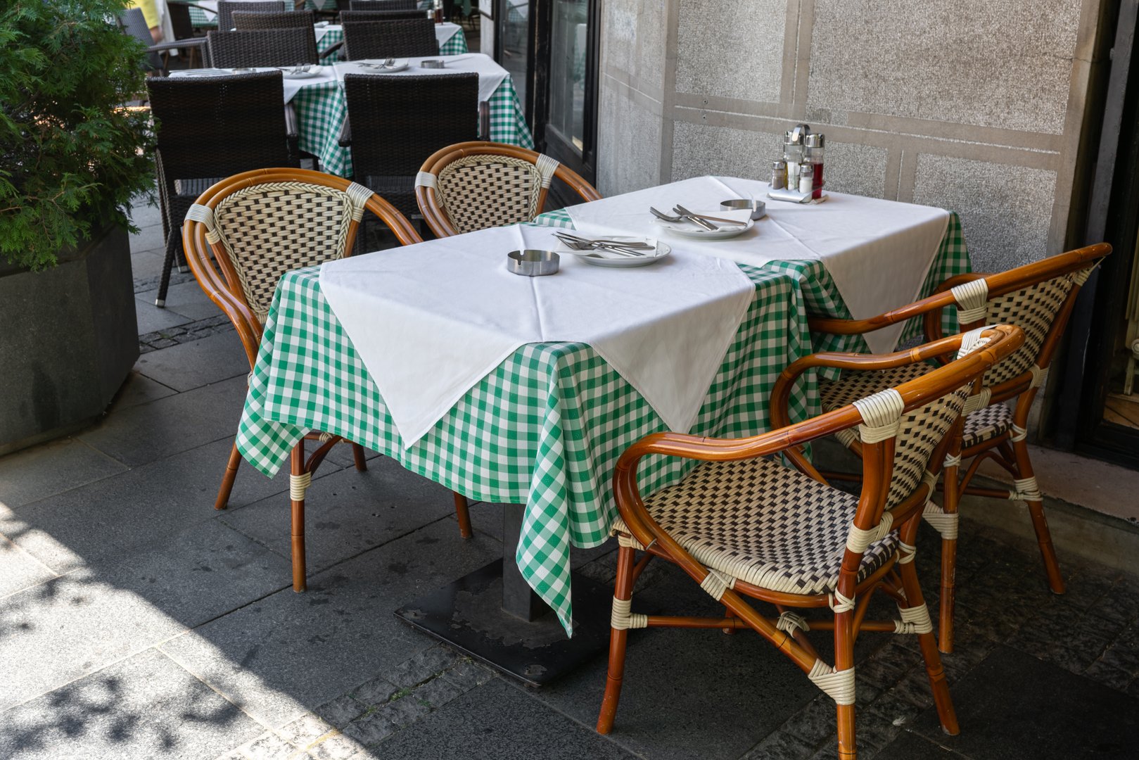 An empty street cafe or restaurant terrace with tables with a traditional mediterranean green checkered tablecloth and wicker chairs, no people.