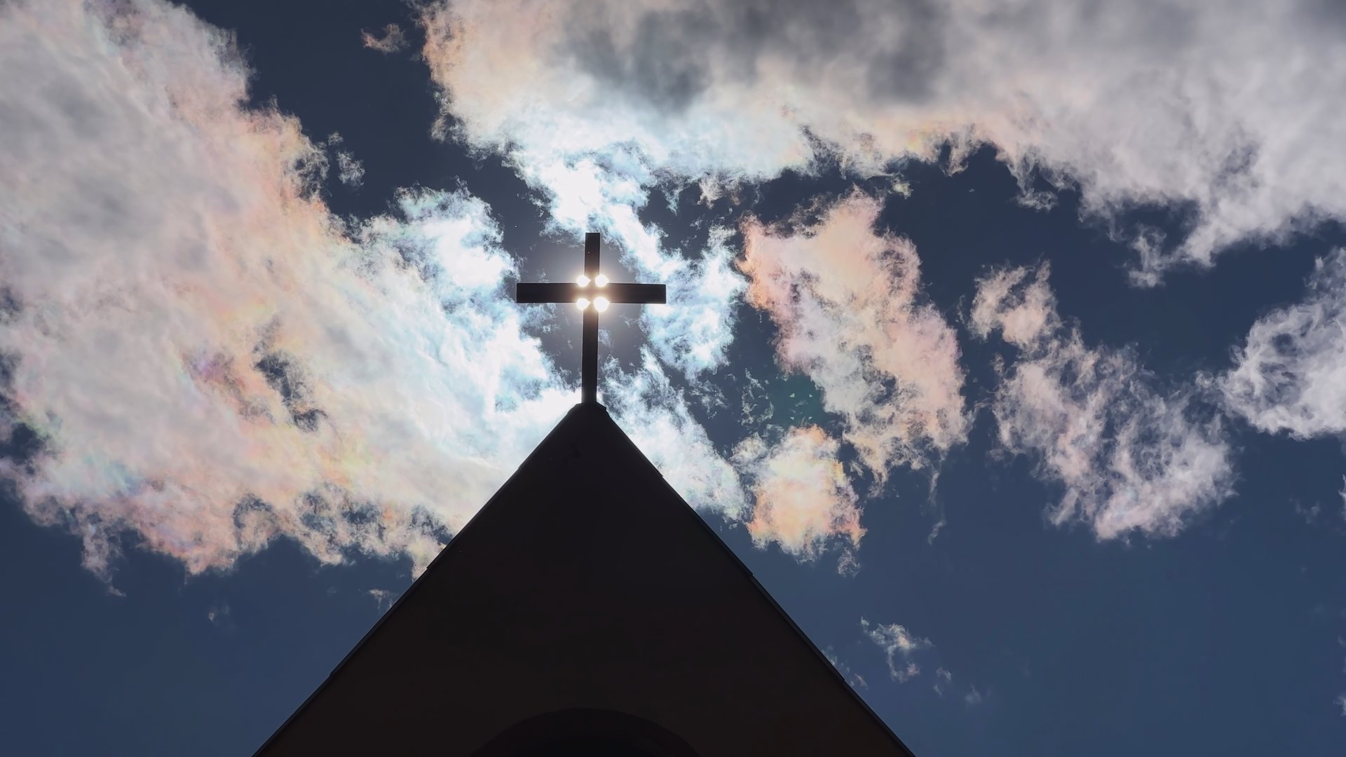 Cross silhouetted against cloudy sky, sunlight illuminating religious symbol, embodying spiritual connection and transcendent belief