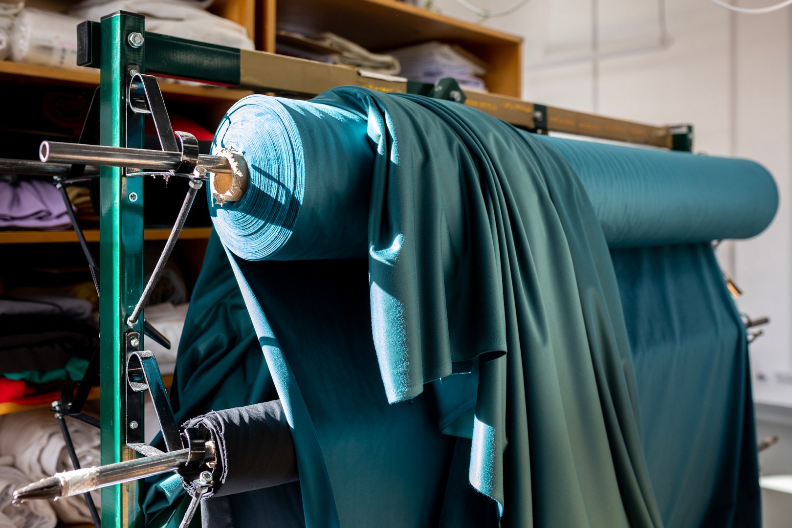 A large roll of teal-colored fabric on an industrial rack in a textile factory or workshop. A concept of the fashion industry, raw materials, and clothing production.