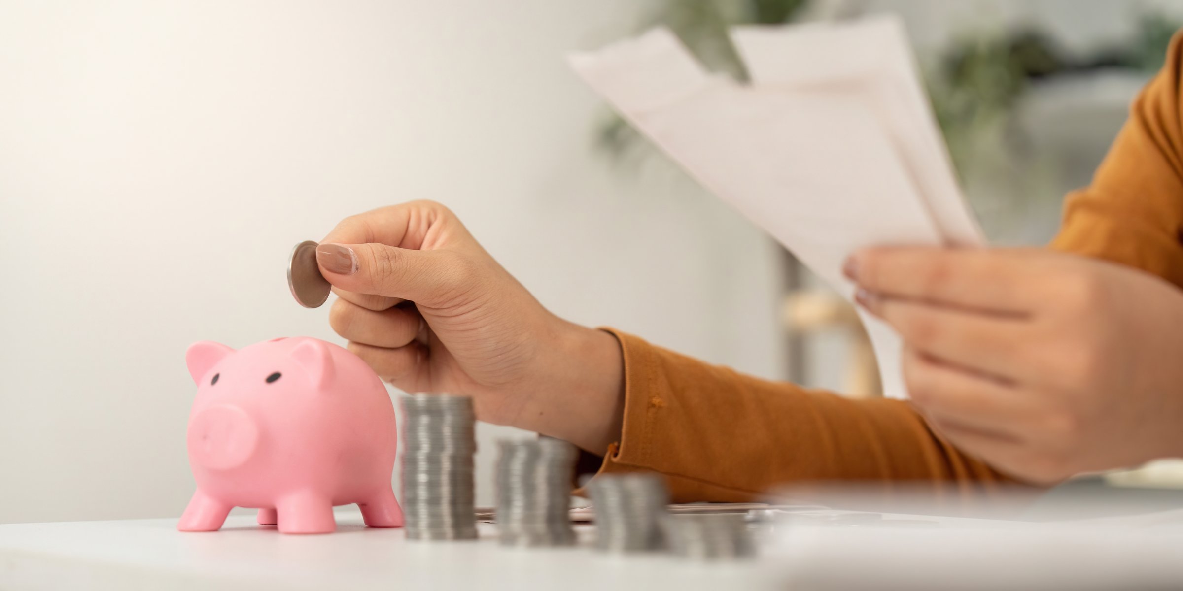 A young woman carefully adding coins to her piggy bank while reviewing her financial documents, emphasizing financial planning.